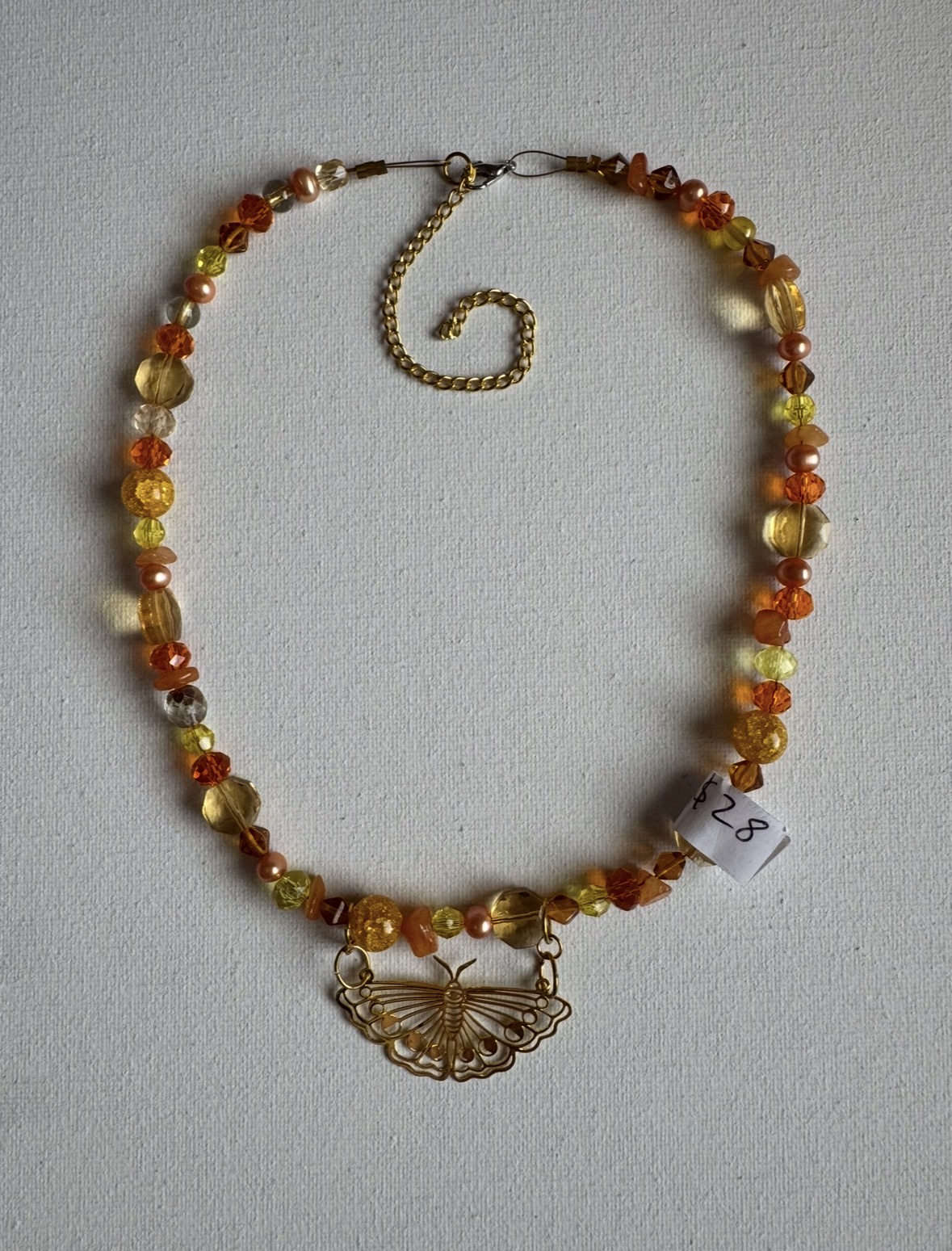 Beaded necklace with a butterfly pendant, featuring orange, yellow, and cream beads, and an adjustable chain.