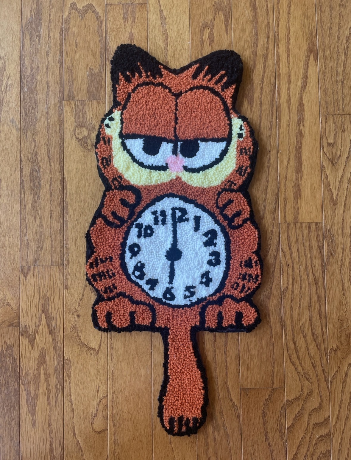 Carpet in the shape of Garfield with a clock on its belly, lying on a wooden floor.