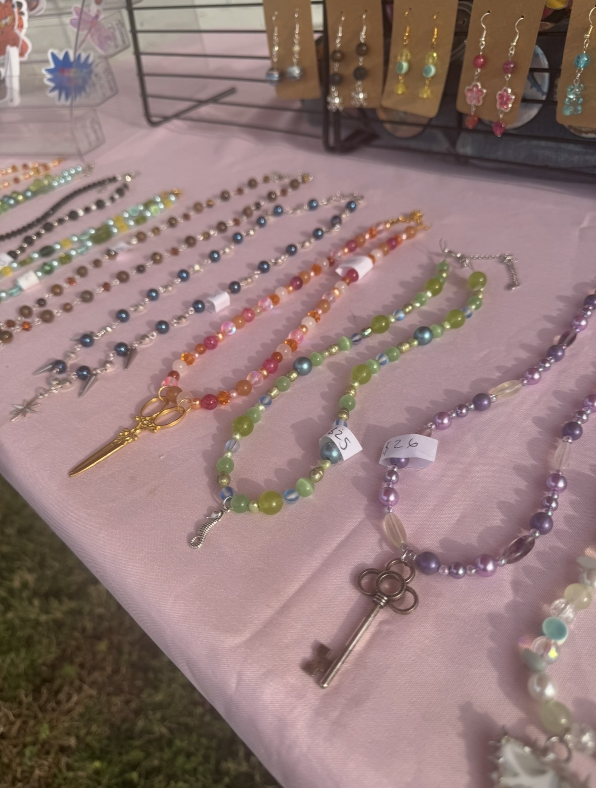 Display of colorful beaded necklaces and jewelry on a pink tablecloth, with earrings and jewelry stands in the background.