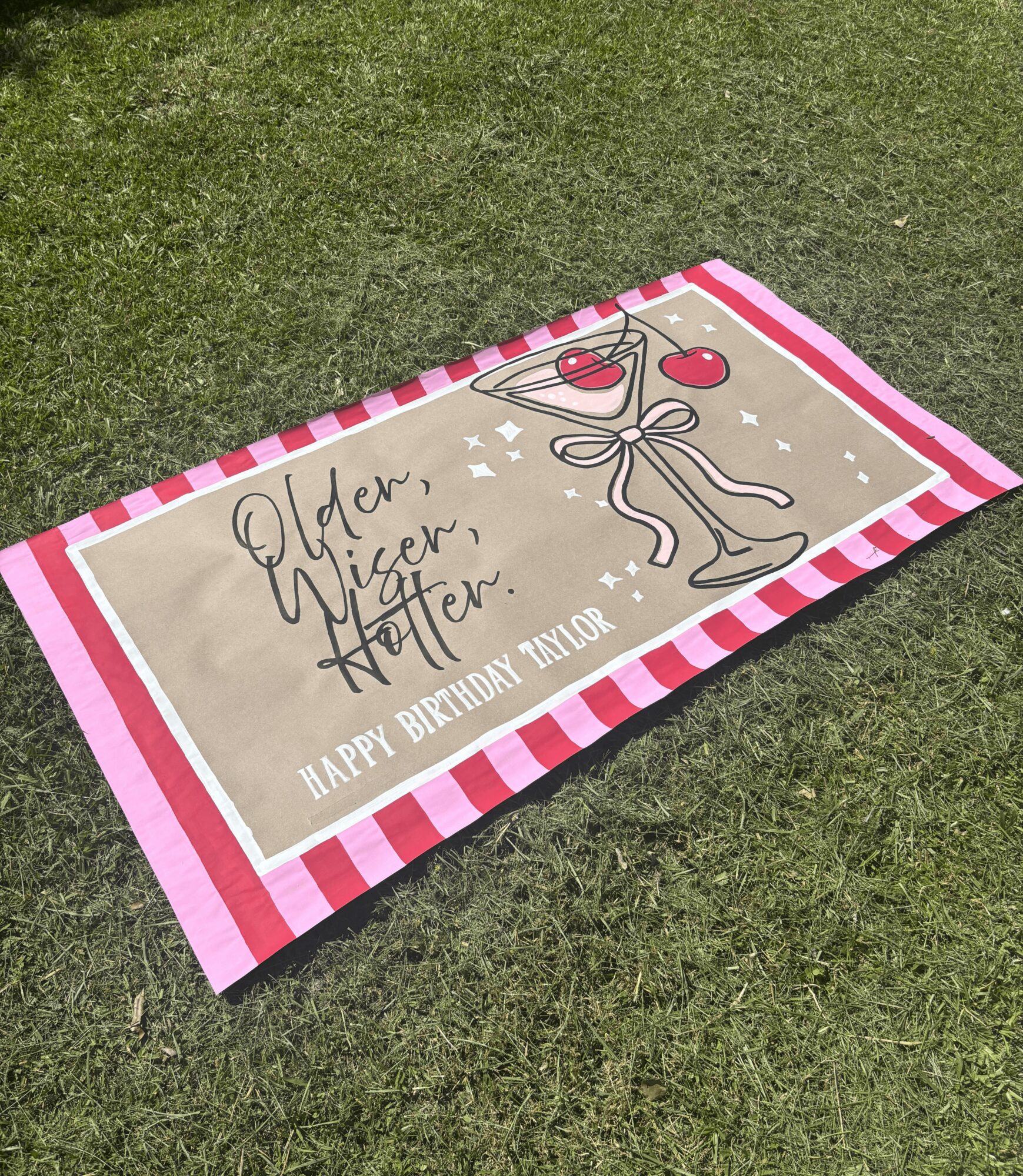 Birthday banner on grass with a glass of wine, a bow, and the text 'Happy Birthday' and 'Aden, Niver, Nater'.