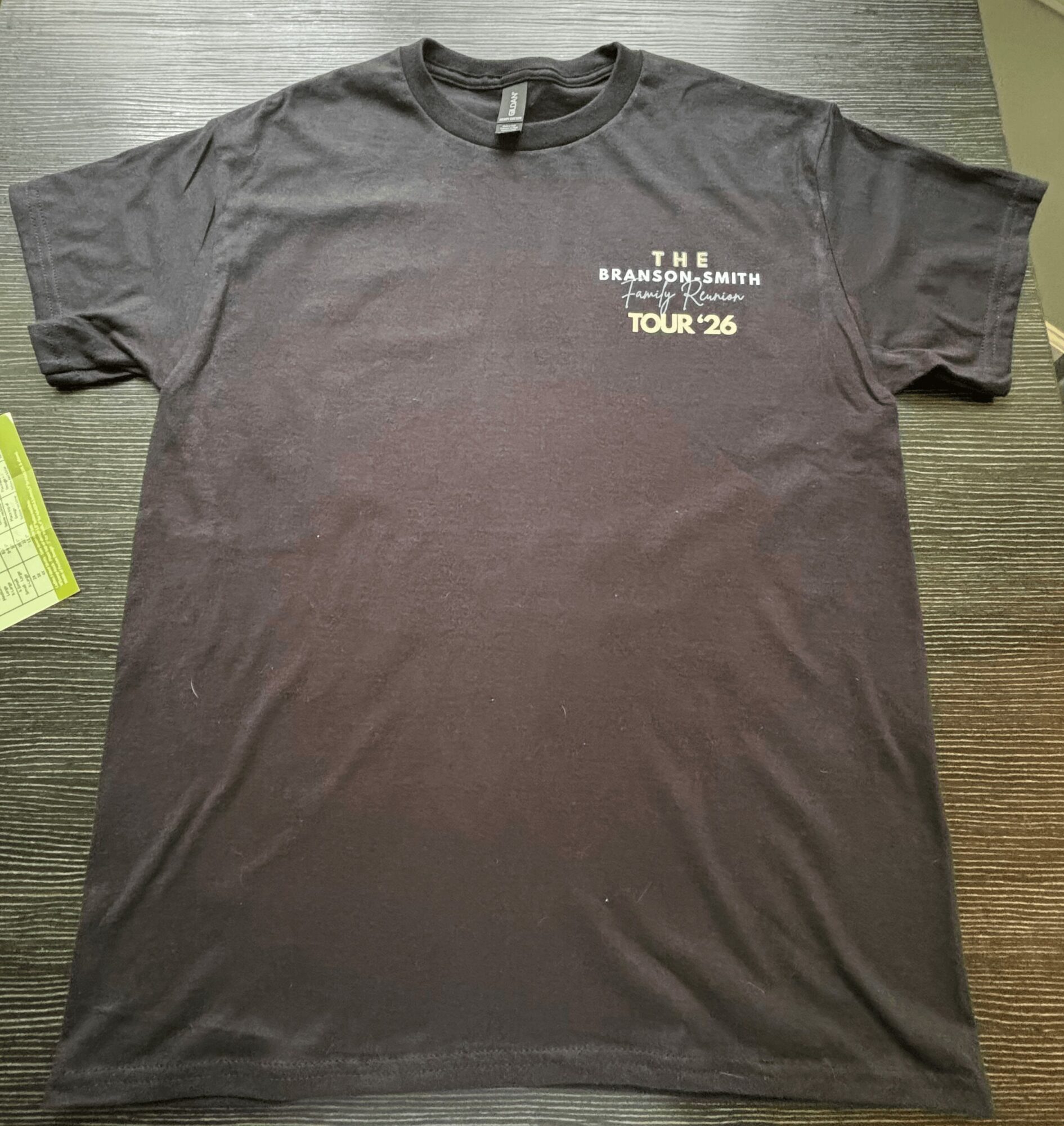 Gray T-shirt with white text on the upper left chest area, laid flat on a surface.