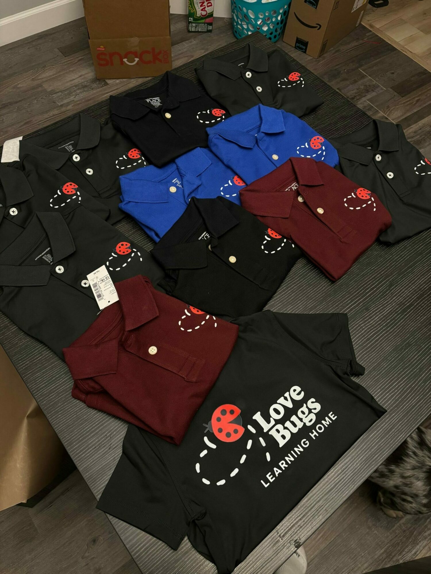 Clothes including black, red, and blue garments with ladybug designs are spread on a gray sofa.