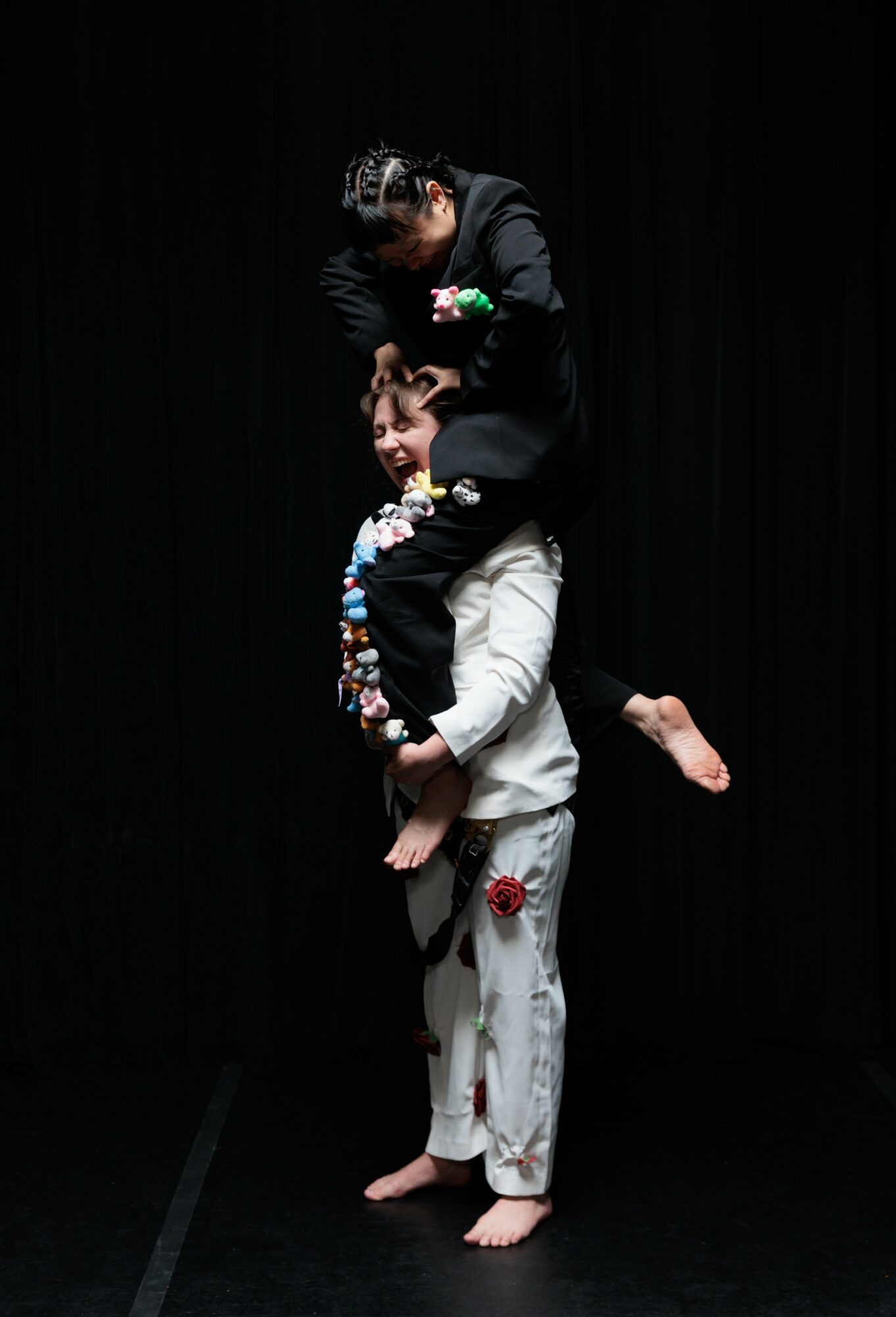 Two children performing a balancing act on stage, one standing and the other sitting on shoulders, against a dark background.
