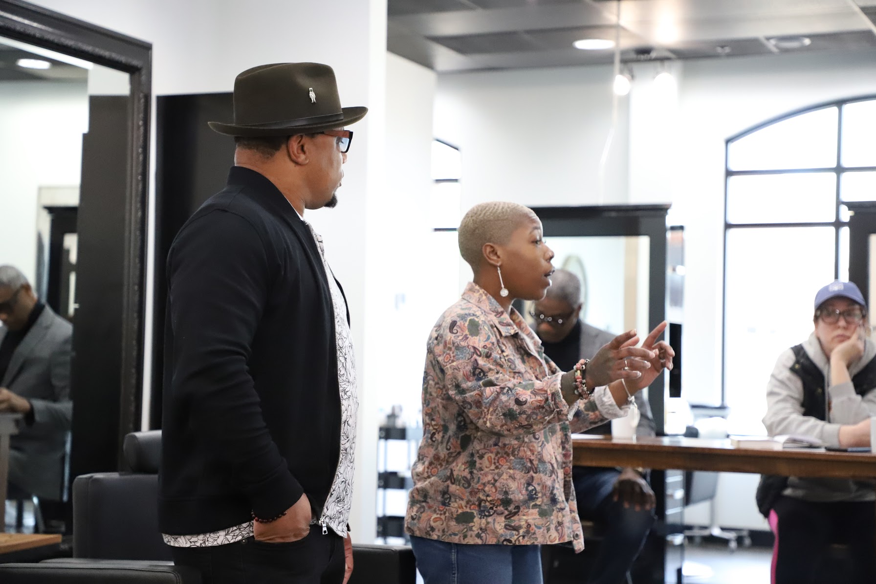 A woman speaking to a group of people in a modern indoor space, with some individuals listening attentively.