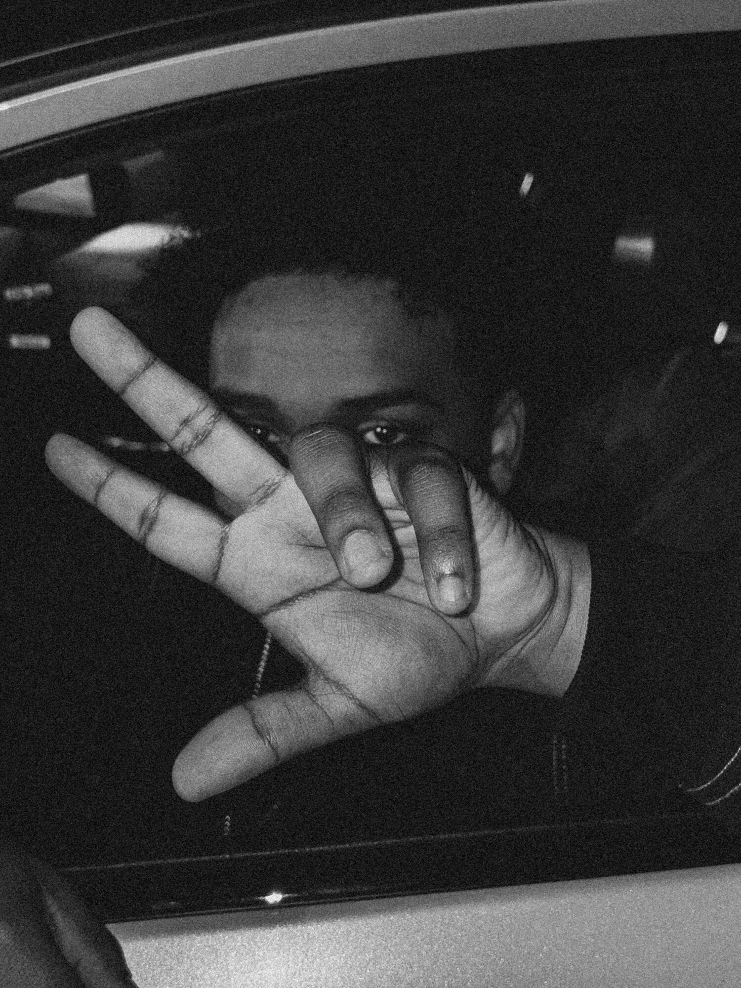 Person's hand making a peace sign near their face, partially covering it, in a dark setting.