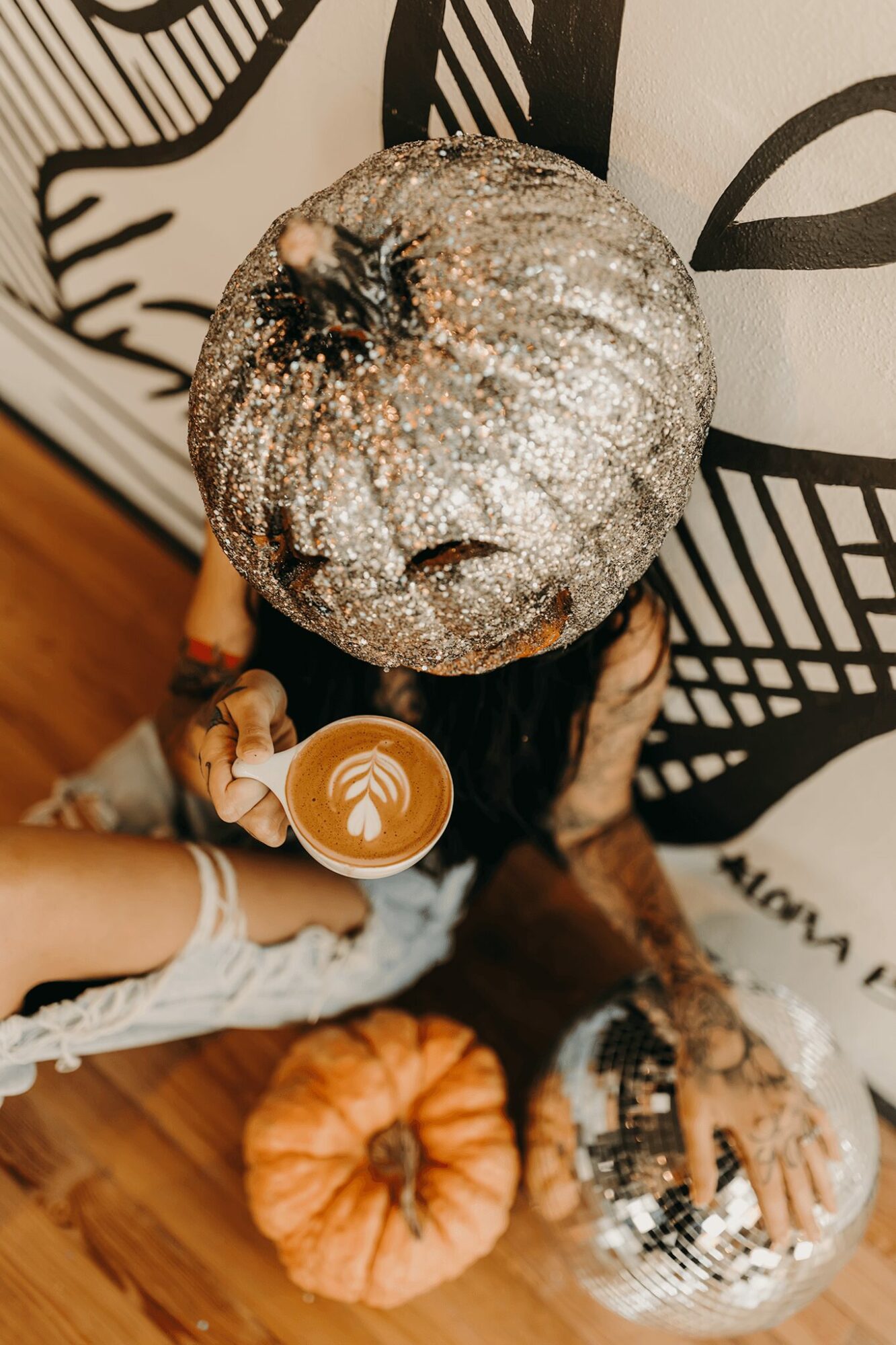 Person holding a coffee cup with latte art, surrounded by pumpkins and decorative items, viewed from above.