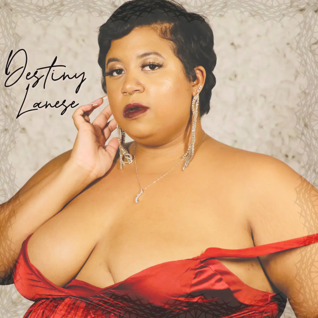 A woman with short black hair and earrings, wearing a red off-shoulder dress, poses with her hand near her face.