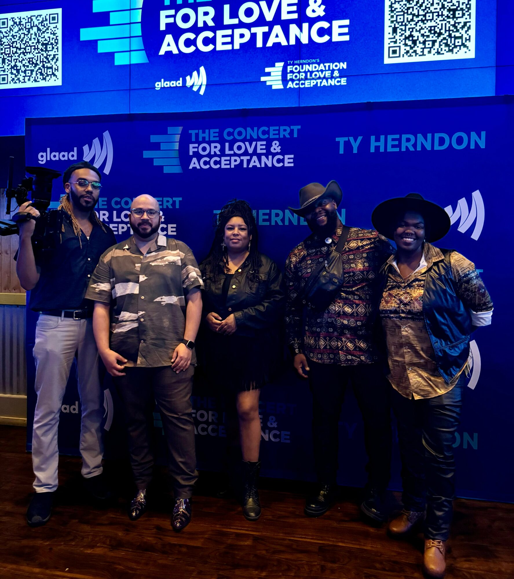 Group of five people standing in front of a blue backdrop with text and logos, smiling and posing for the photo.