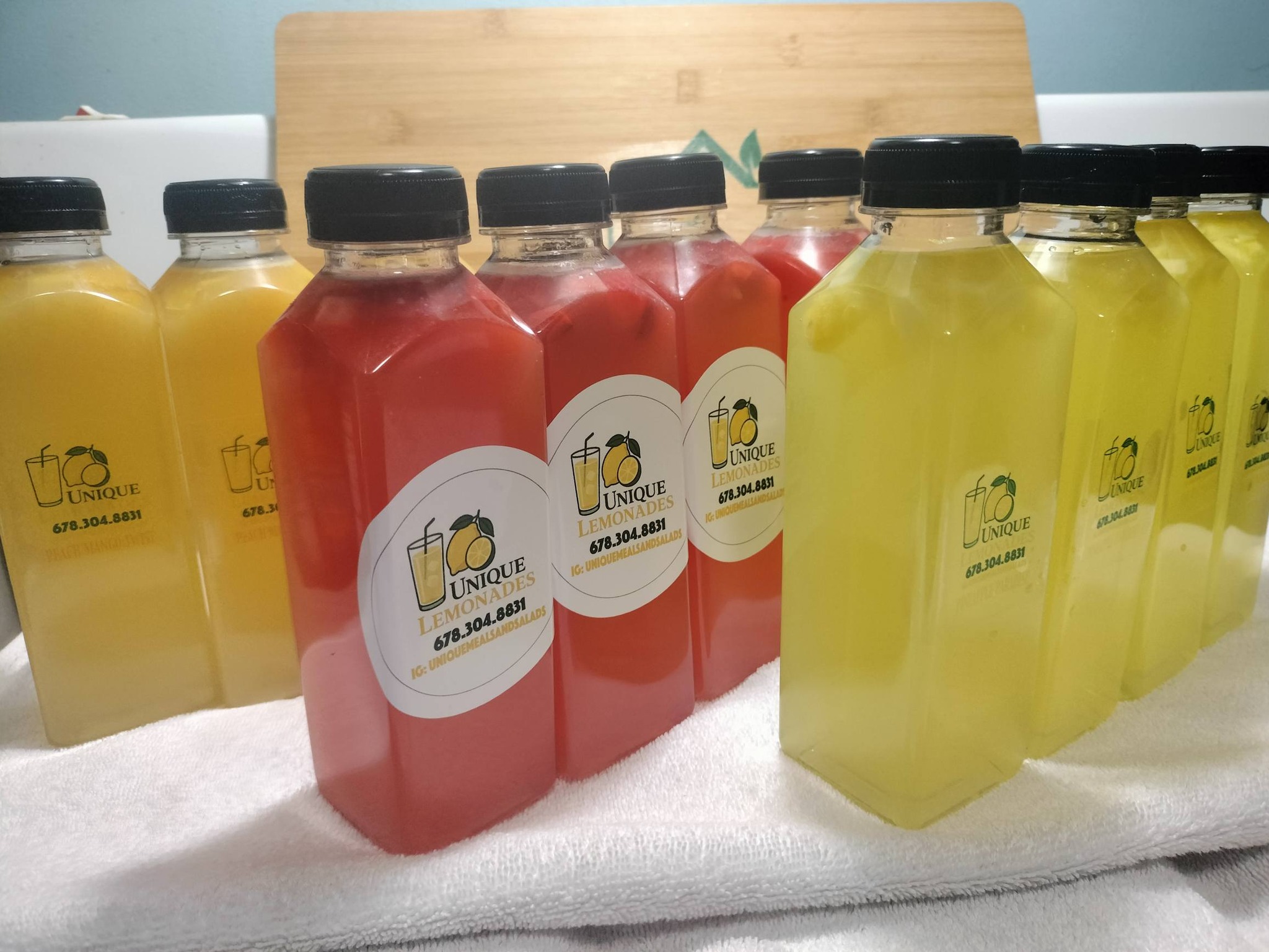 Bottles of yellow and red beverages with labels, arranged on a white cloth, with a wooden background.