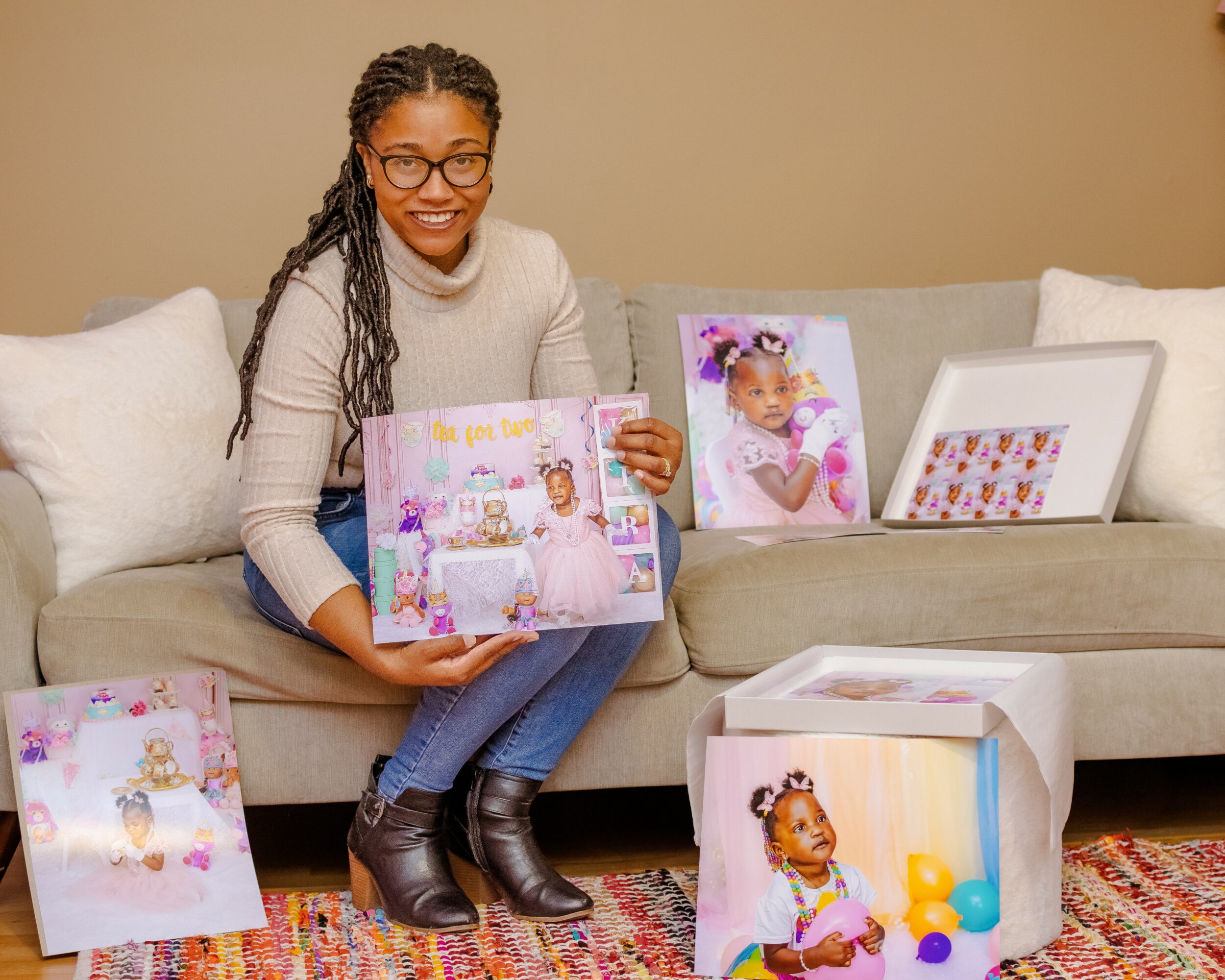 Woman sitting on sofa holding a colorful scrapbook, with framed photos and a box of toys nearby, in a living room.