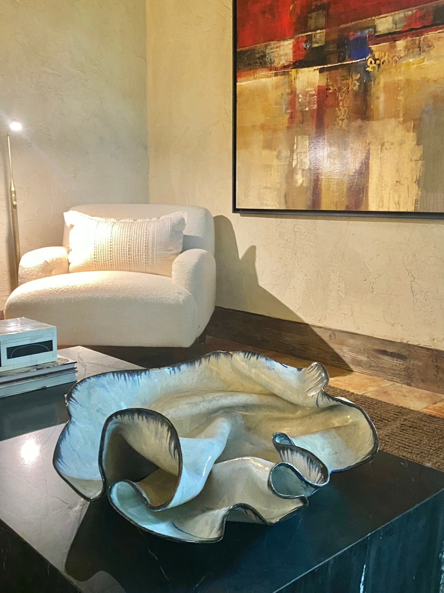 Living room with a white sofa, a large abstract painting, and a decorative ceramic bowl on a dark table.