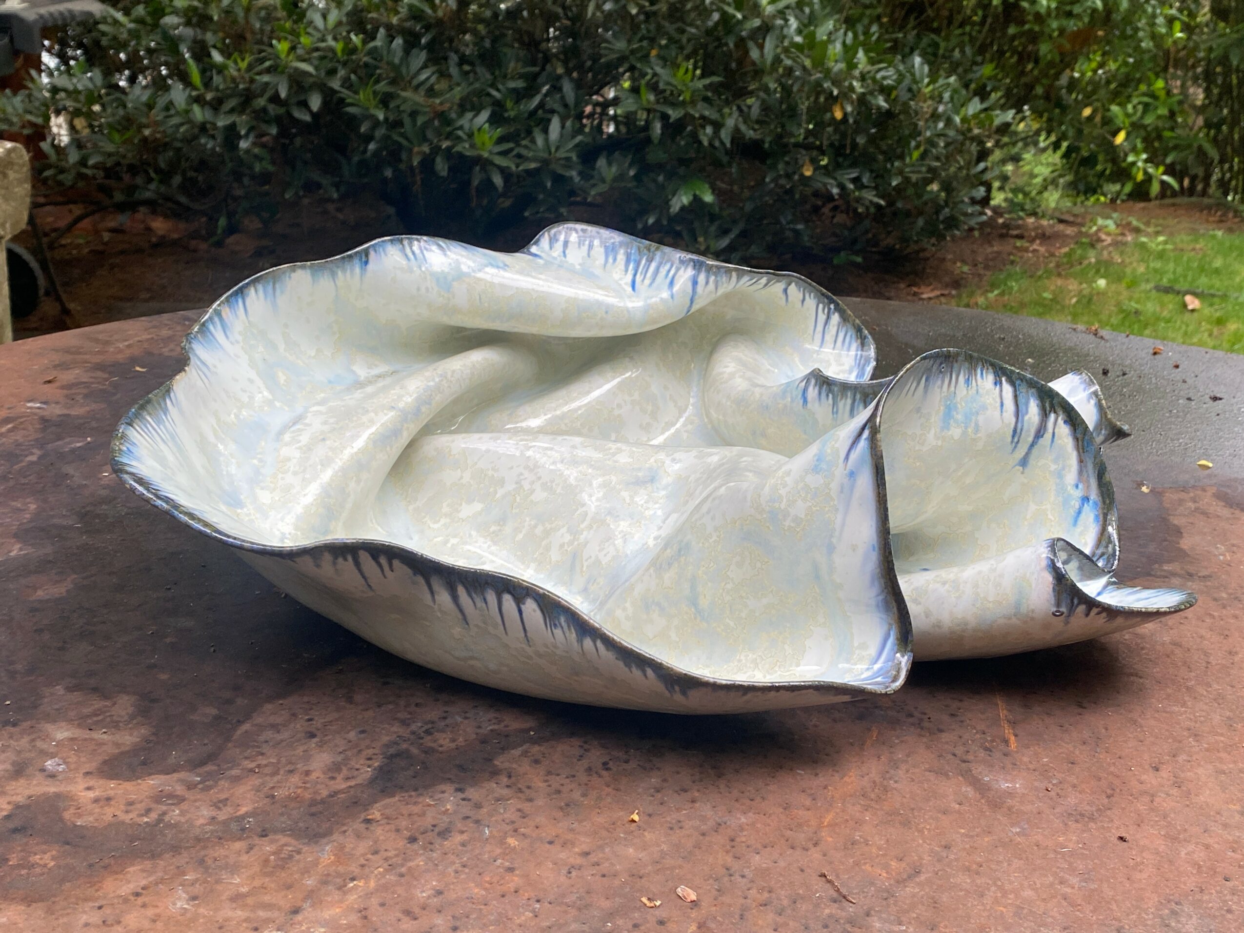 Cream-colored ceramic dish with blue accents, irregular shape, and a small handle on one side, placed on a wooden surface.