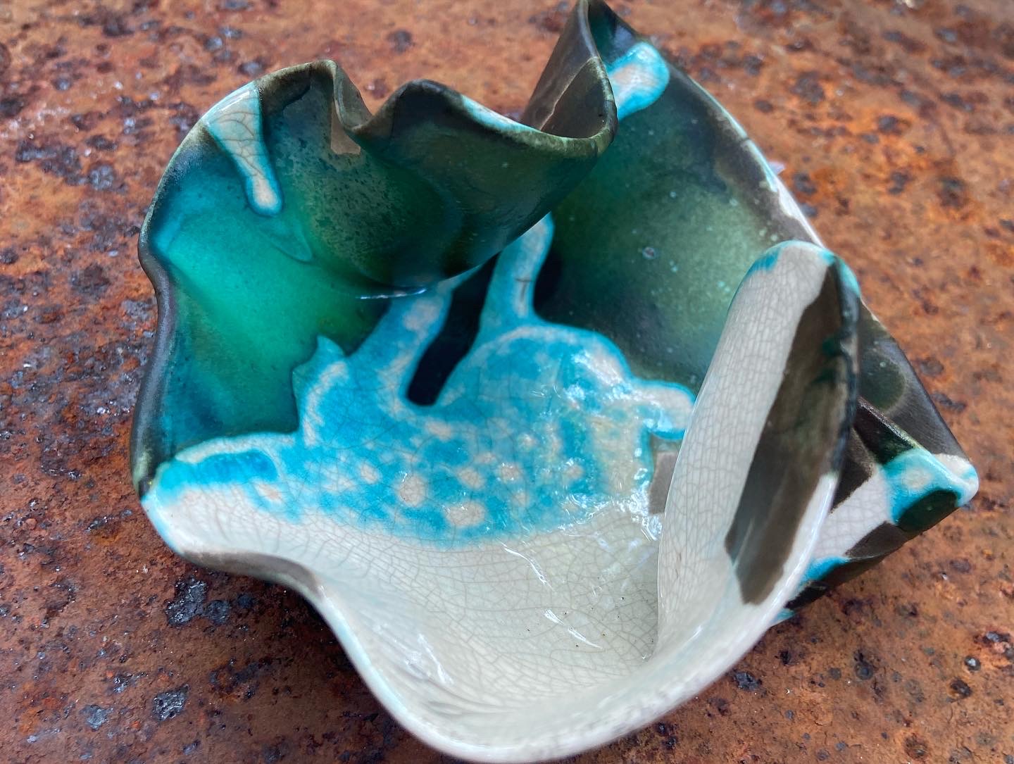 Small ceramic bowl with blue, green, and white glaze, placed on a textured brown surface.