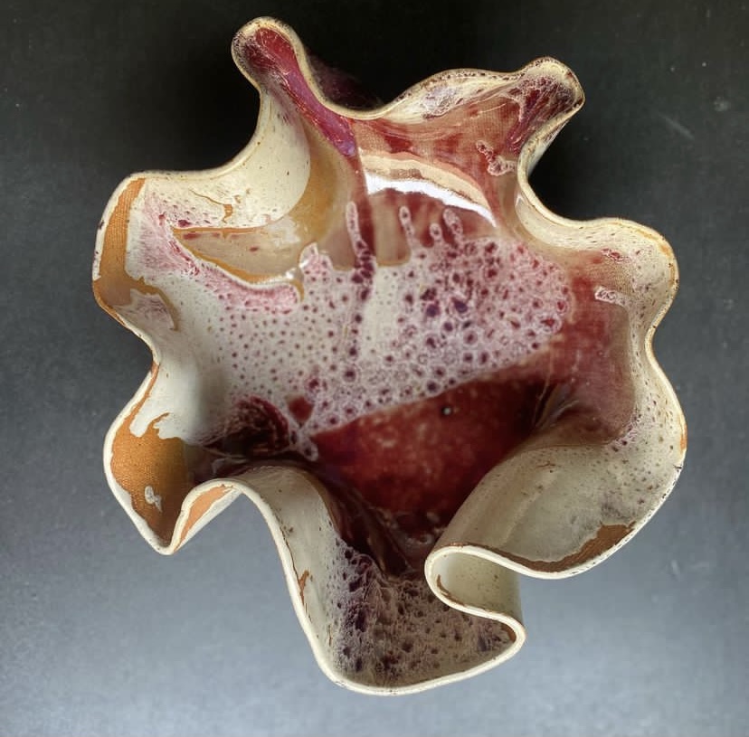 A ceramic bowl with irregular, wavy edges, filled with a red and white liquid, on a dark surface.