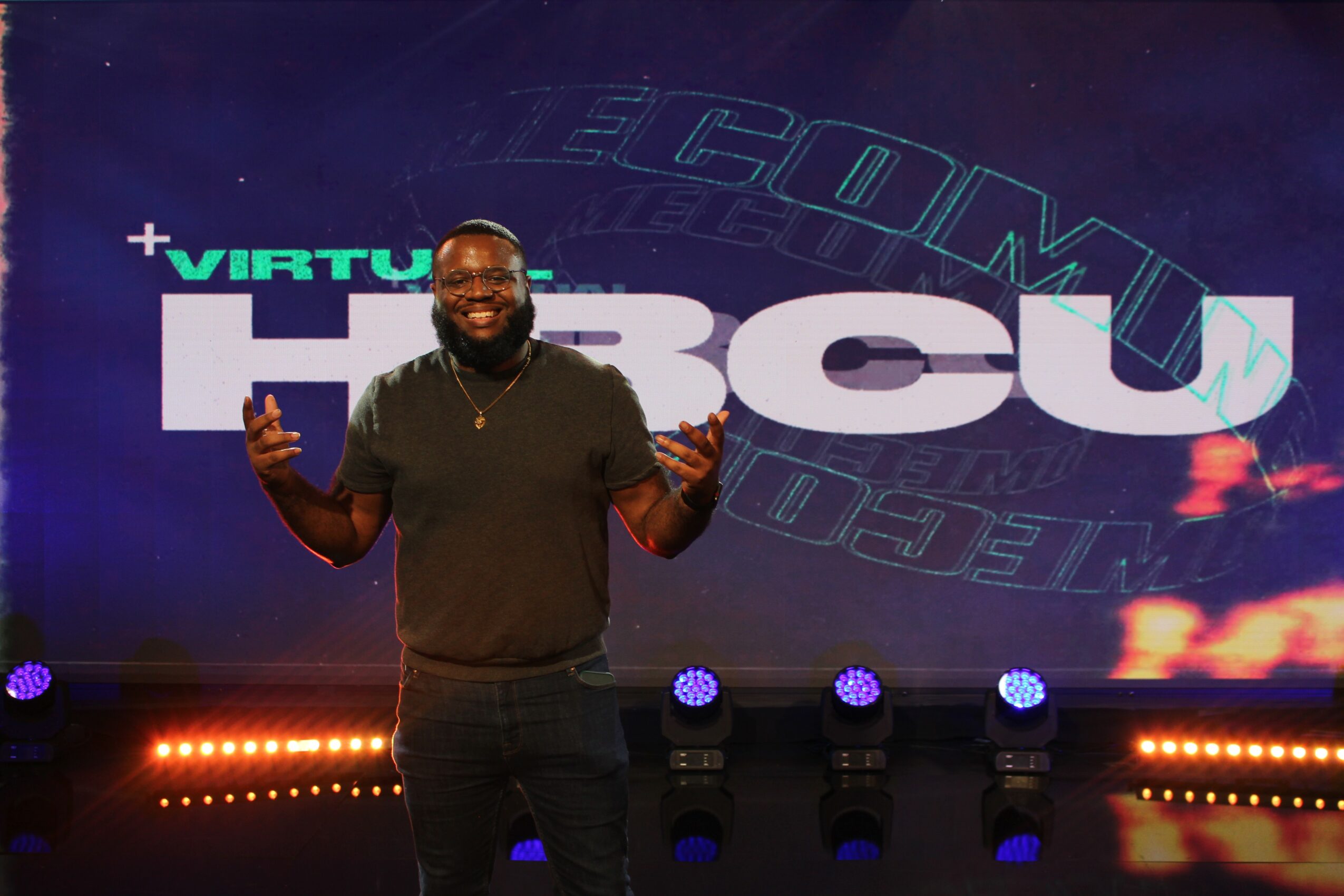 Man smiling and gesturing in front of a large screen with the text 'VIRTU' and 'HBCU'.
