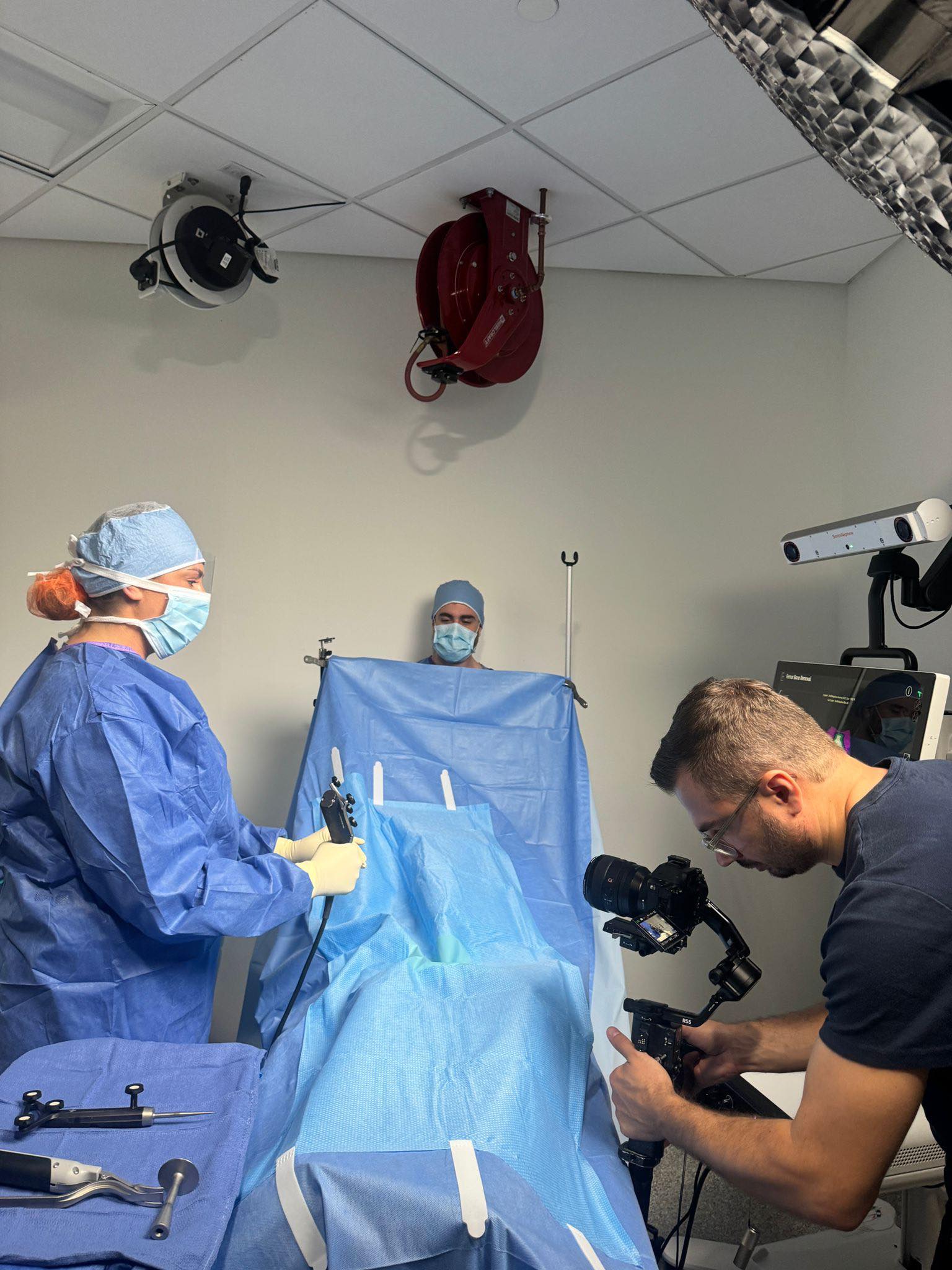 Medical team in operating room preparing for surgery, with a camera operator filming the scene.