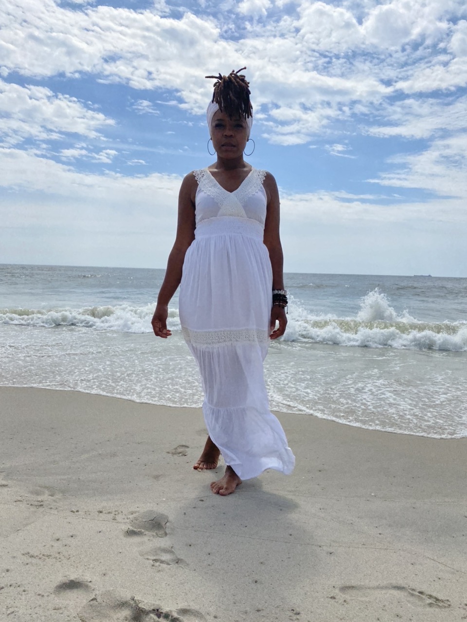 Woman in white dress walking on beach with ocean and sky in background