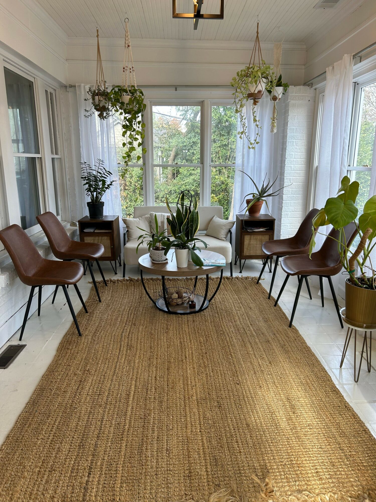 Living room with large windows, plants, a white sofa, and a beige rug, viewed from the side.