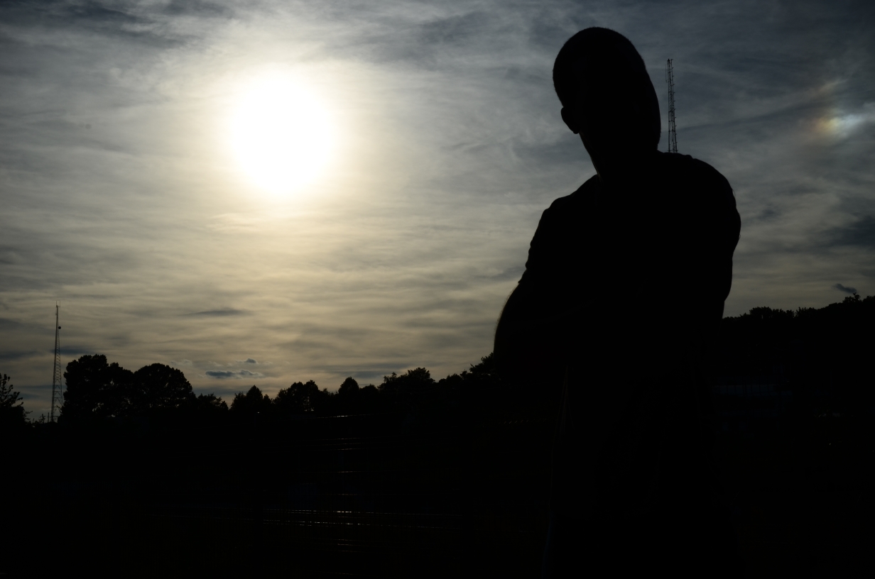 Silhouette of a person outdoors with a bright sun and cloudy sky in the background.