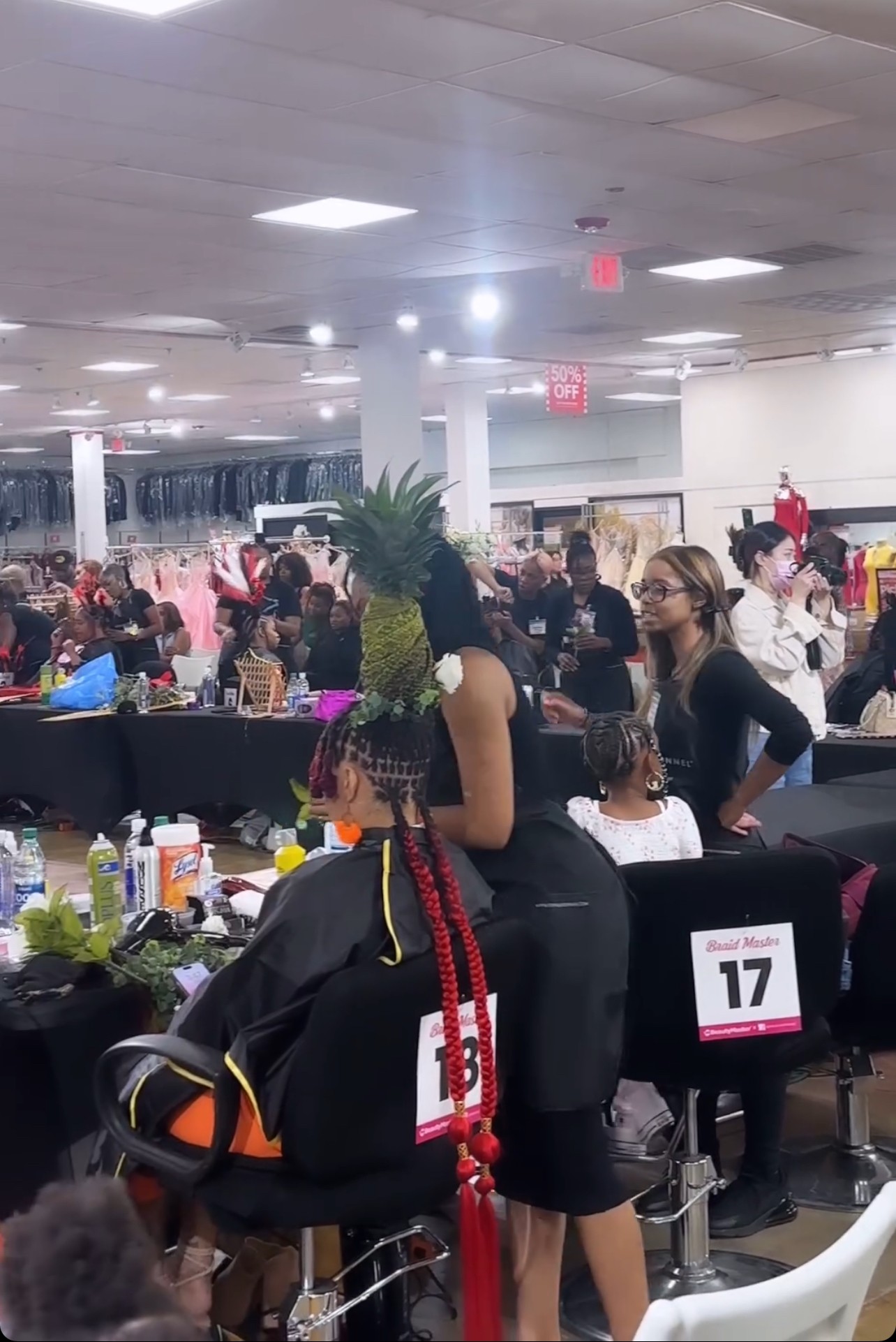 Person wearing a pineapple costume with a pineapple headpiece, standing in a busy indoor shopping area or event space.