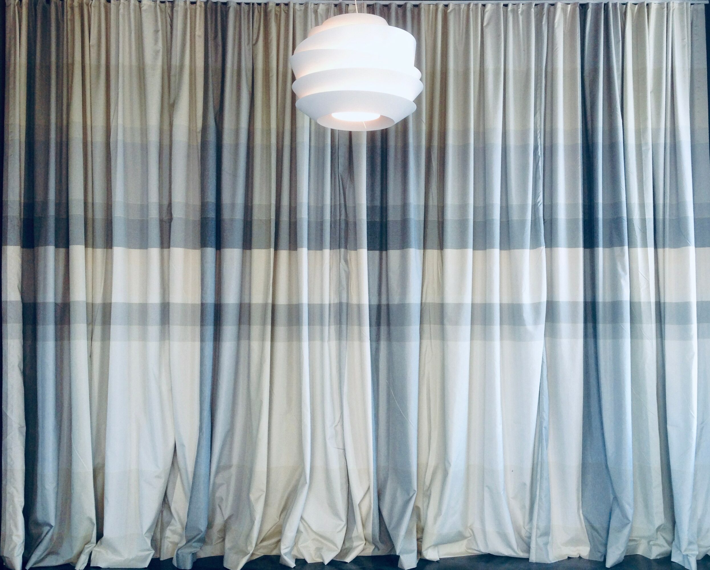 Curtains with a hanging ceiling light in front, neutral colors, soft lighting, and a textured fabric appearance.
