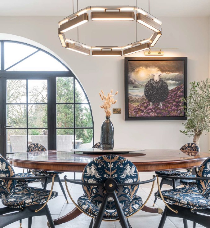 Interior dining room with large window, round table, decorative chairs, a painting, and a modern chandelier.