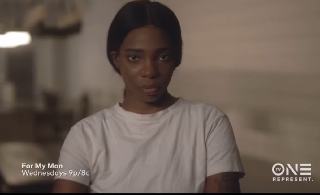 Young woman with short dark hair wearing a white T-shirt, looking at the camera, in a room with neutral background.