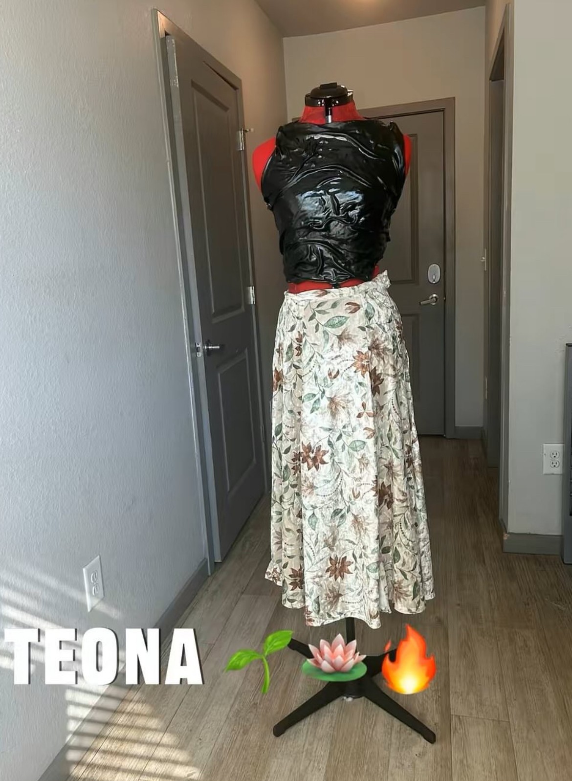 Person wearing a black jacket and floral skirt standing in a hallway with closed doors, facing away from the camera.