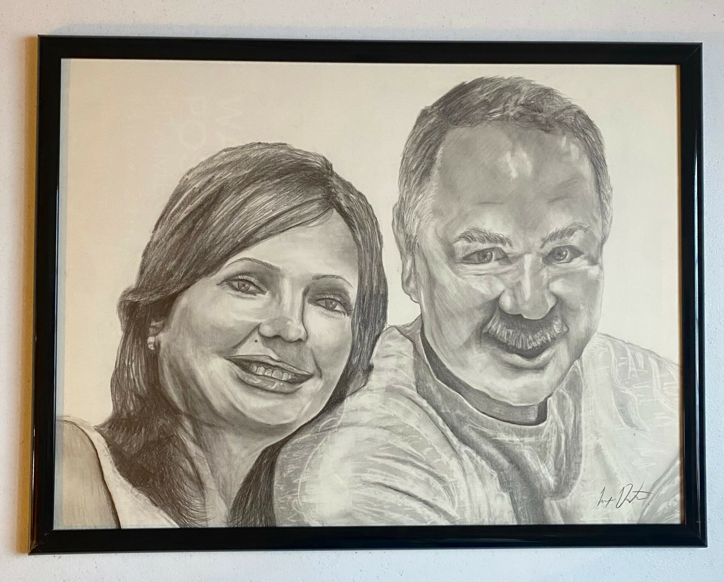 Black and white portrait of a smiling woman and man, framed on a wall.