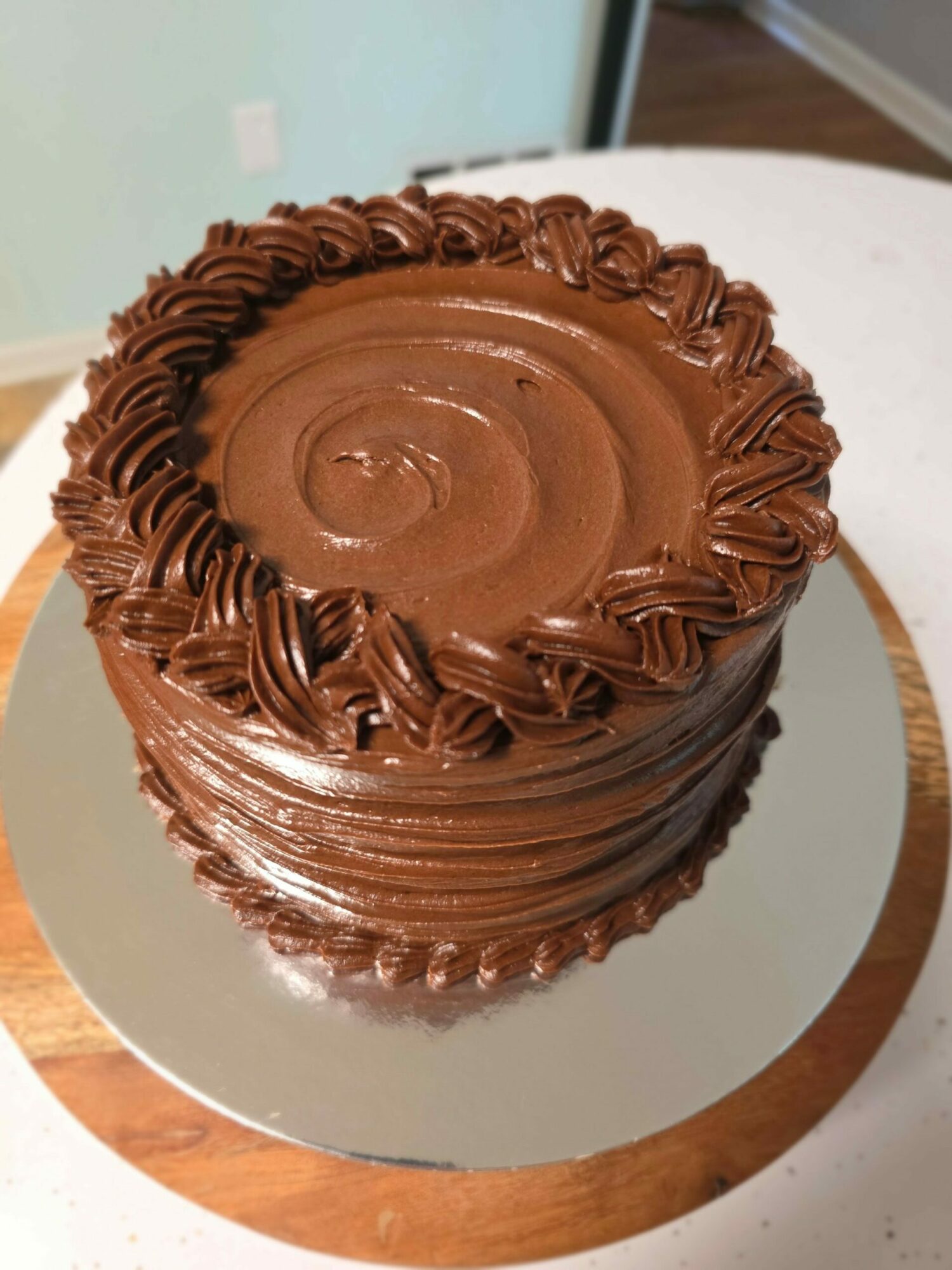 Chocolate cake with decorative frosting, viewed from the top, on a round mirror surface with a wooden base.