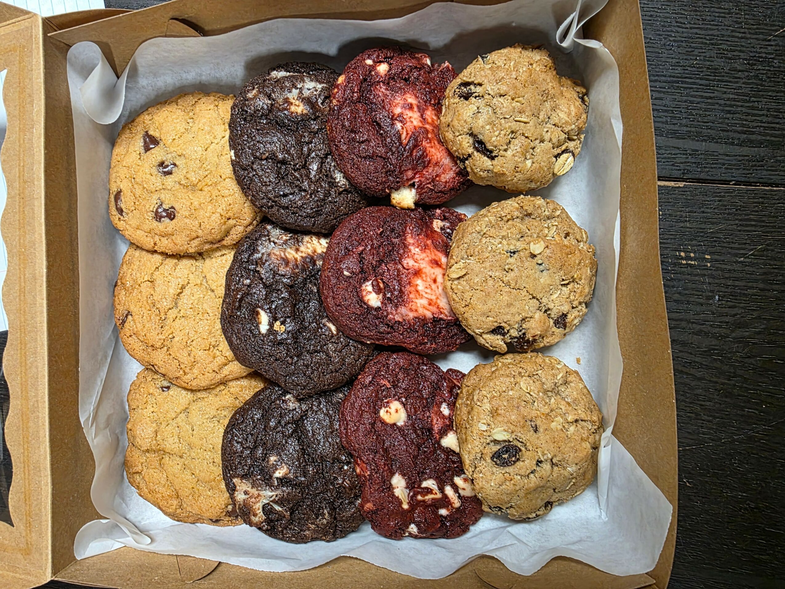 Box of assorted cookies with chocolate chip, double chocolate, and oatmeal raisin varieties, arranged in three rows.