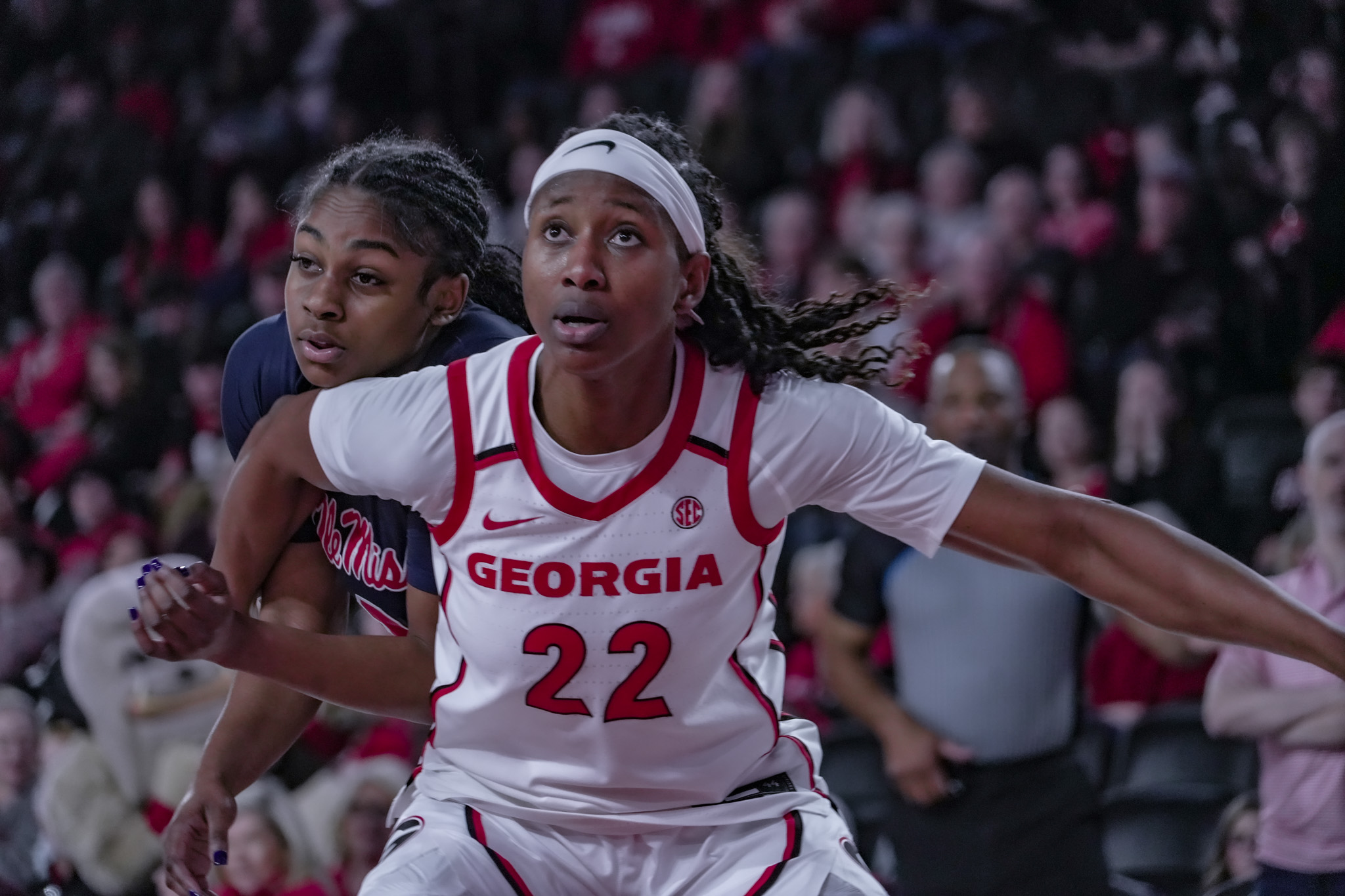 Two female basketball players in action during a game, one wearing a Georgia jersey with number 22, crowd in background.