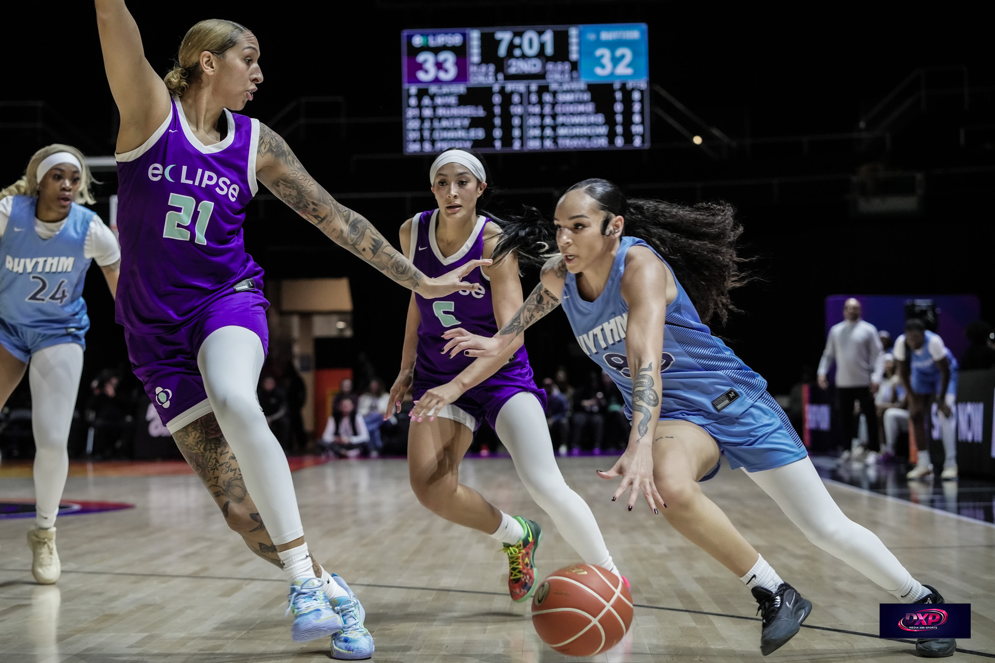 Three female basketball players compete for the ball on the court, with a scoreboard in the background showing 7:01 and scores 33 and 32.