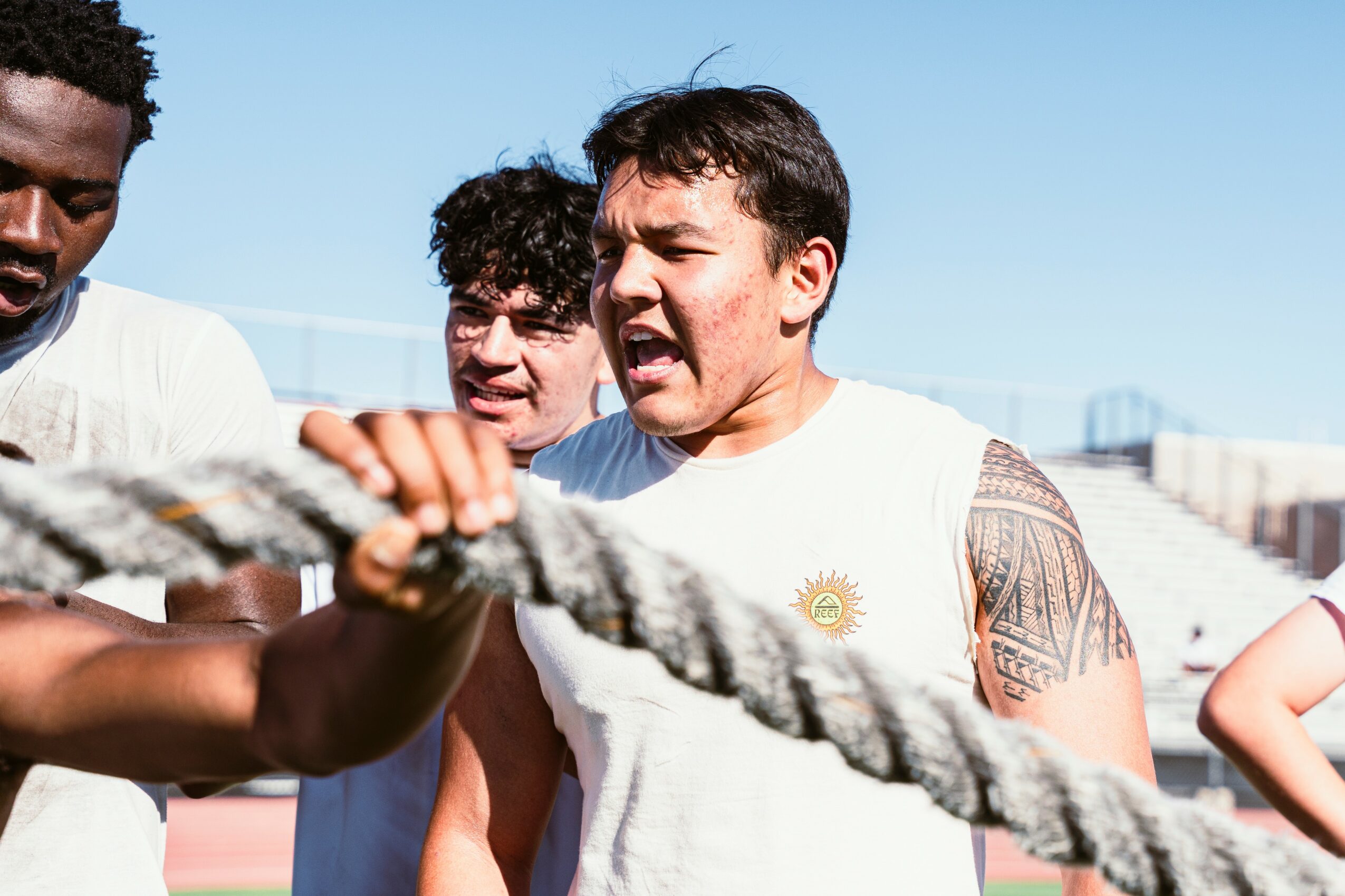 Three people outdoors holding a thick rope, with a clear blue sky in the background.