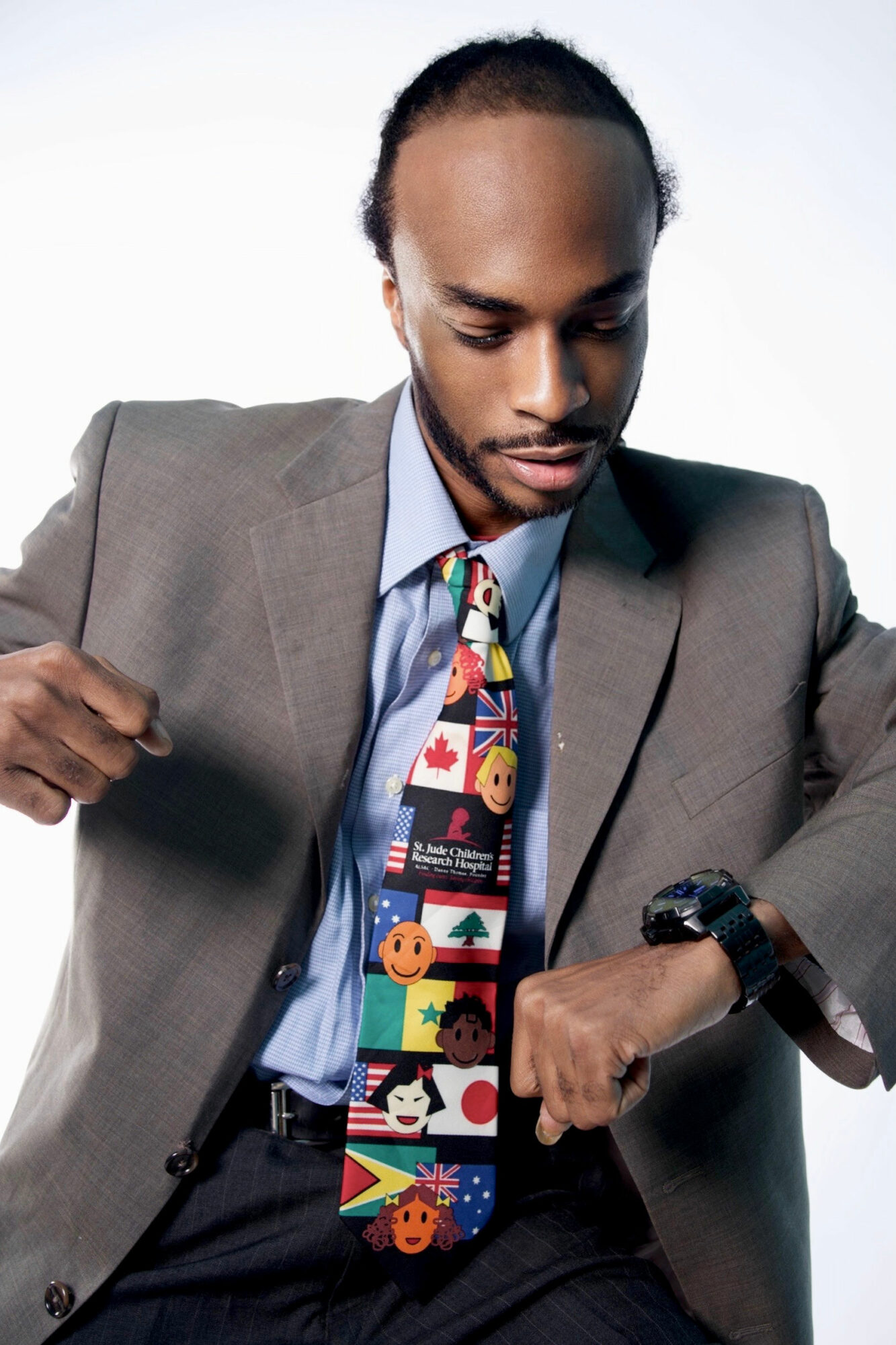 Man in suit adjusting his watch, wearing a colorful tie, against a plain background.