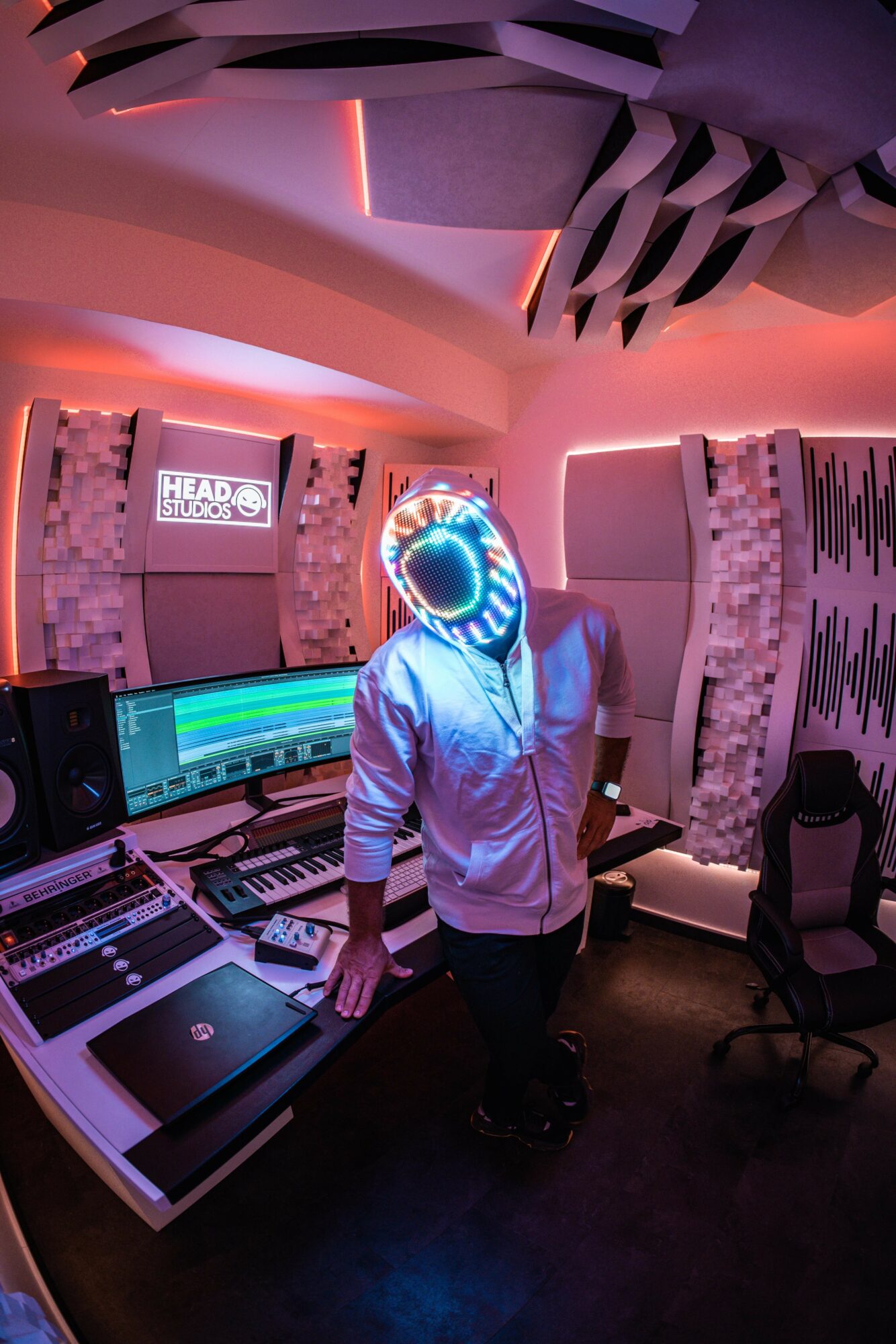 Person wearing a glowing headset in a music studio with equipment and colorful lighting.