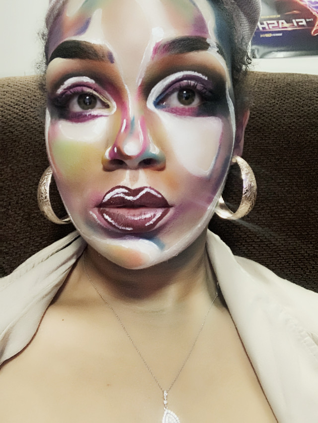 Person with colorful face paint, large earrings, and makeup, sitting on a brown couch.