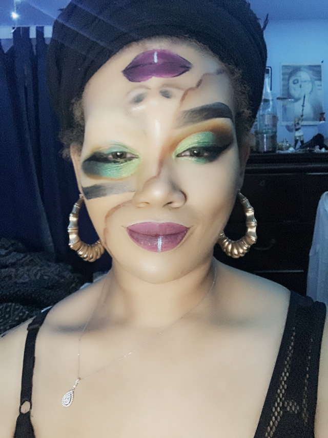 Woman with makeup, large hoop earrings, black headwrap, and a necklace, smiling in a room with blue lighting.