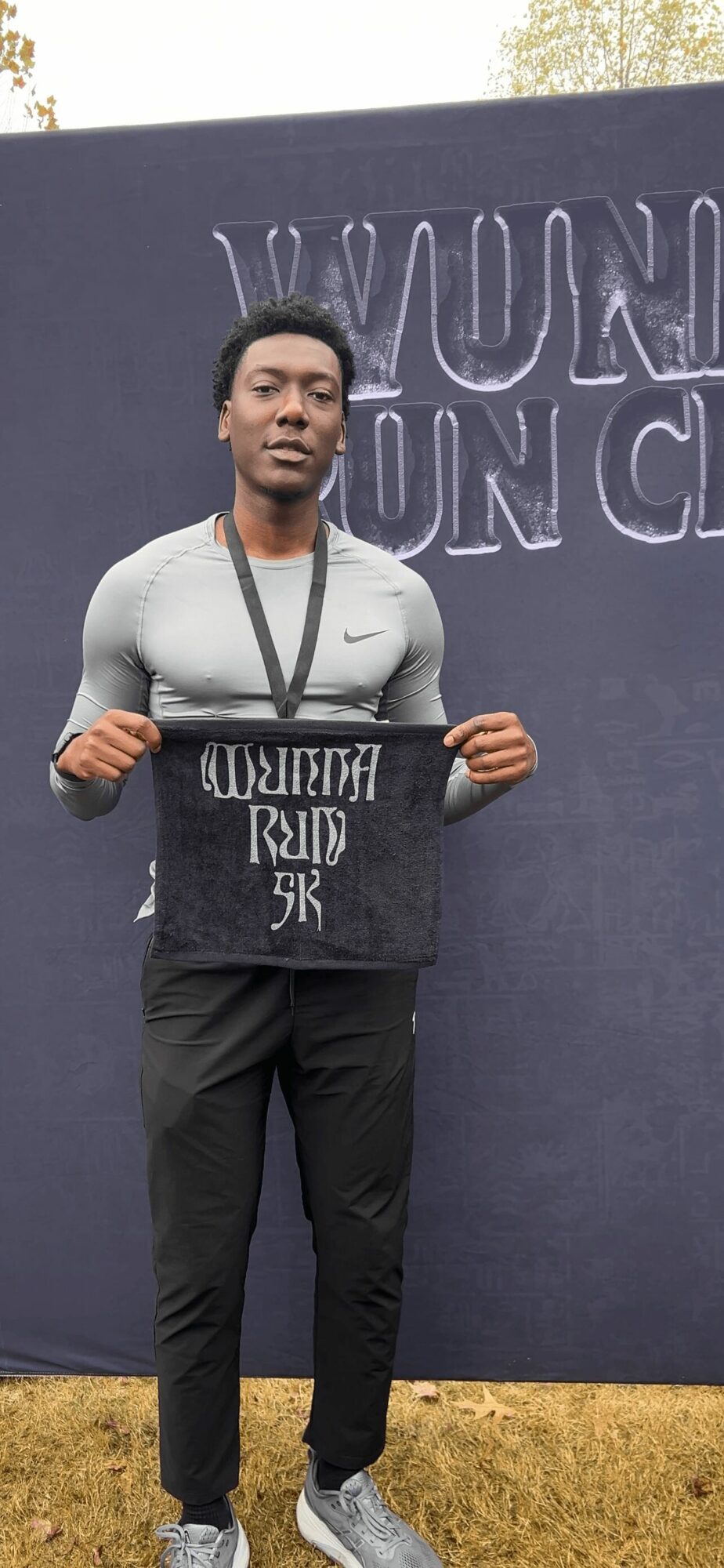 Person holding a sign in front of a large dark blue background with text, outdoors, grass visible at bottom.