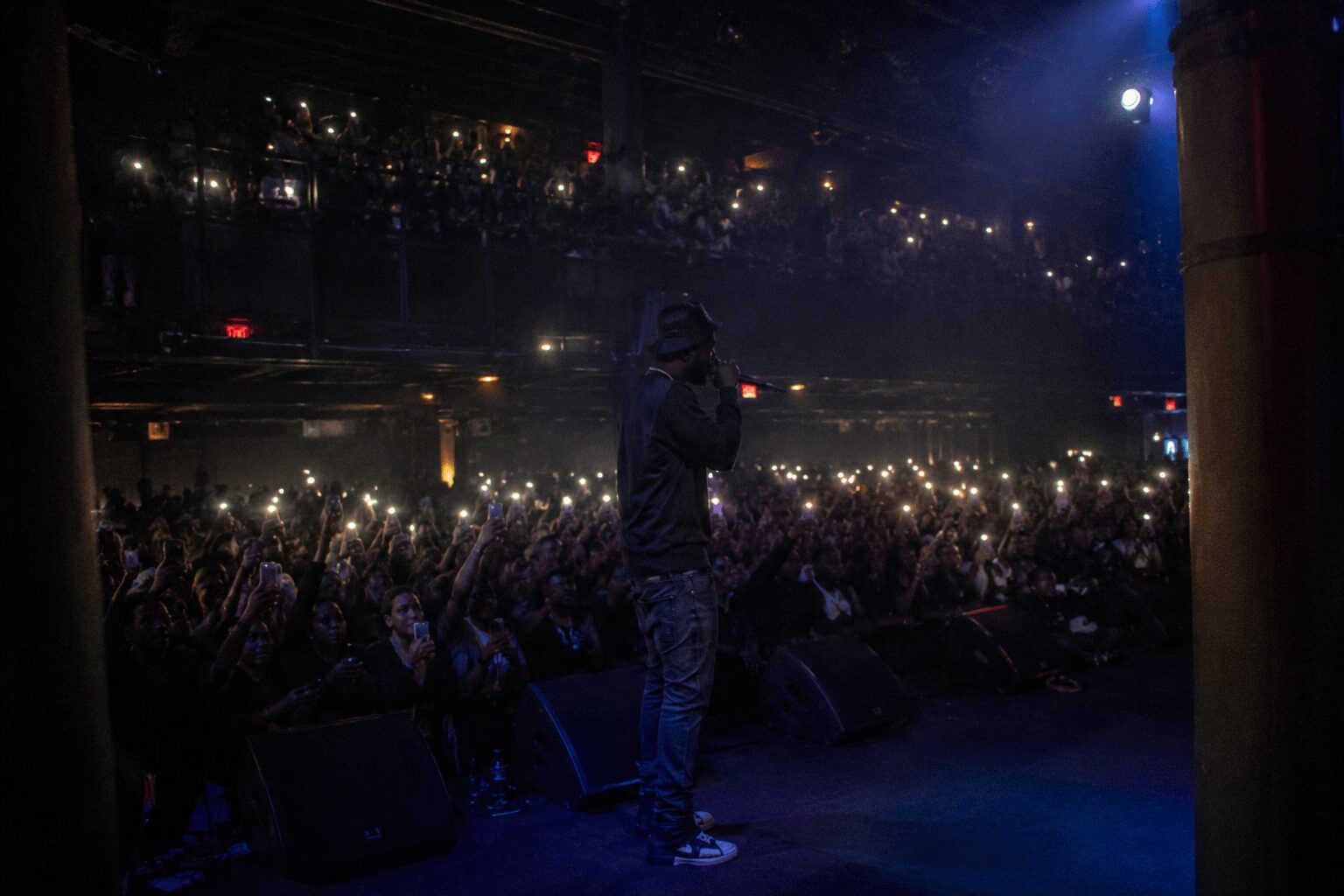 Performer on stage with audience holding up lights in a dark, indoor concert venue.