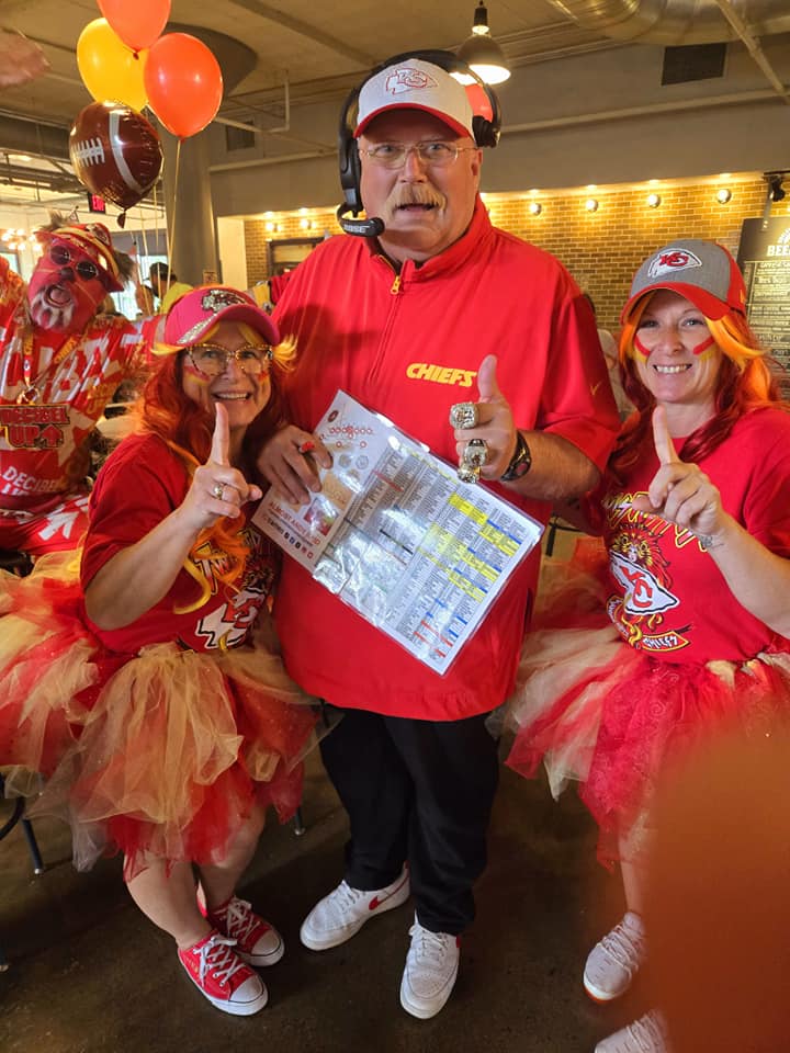 Three people in Kansas City Chiefs attire, two women and one man, celebrating indoors with balloons and decorations.