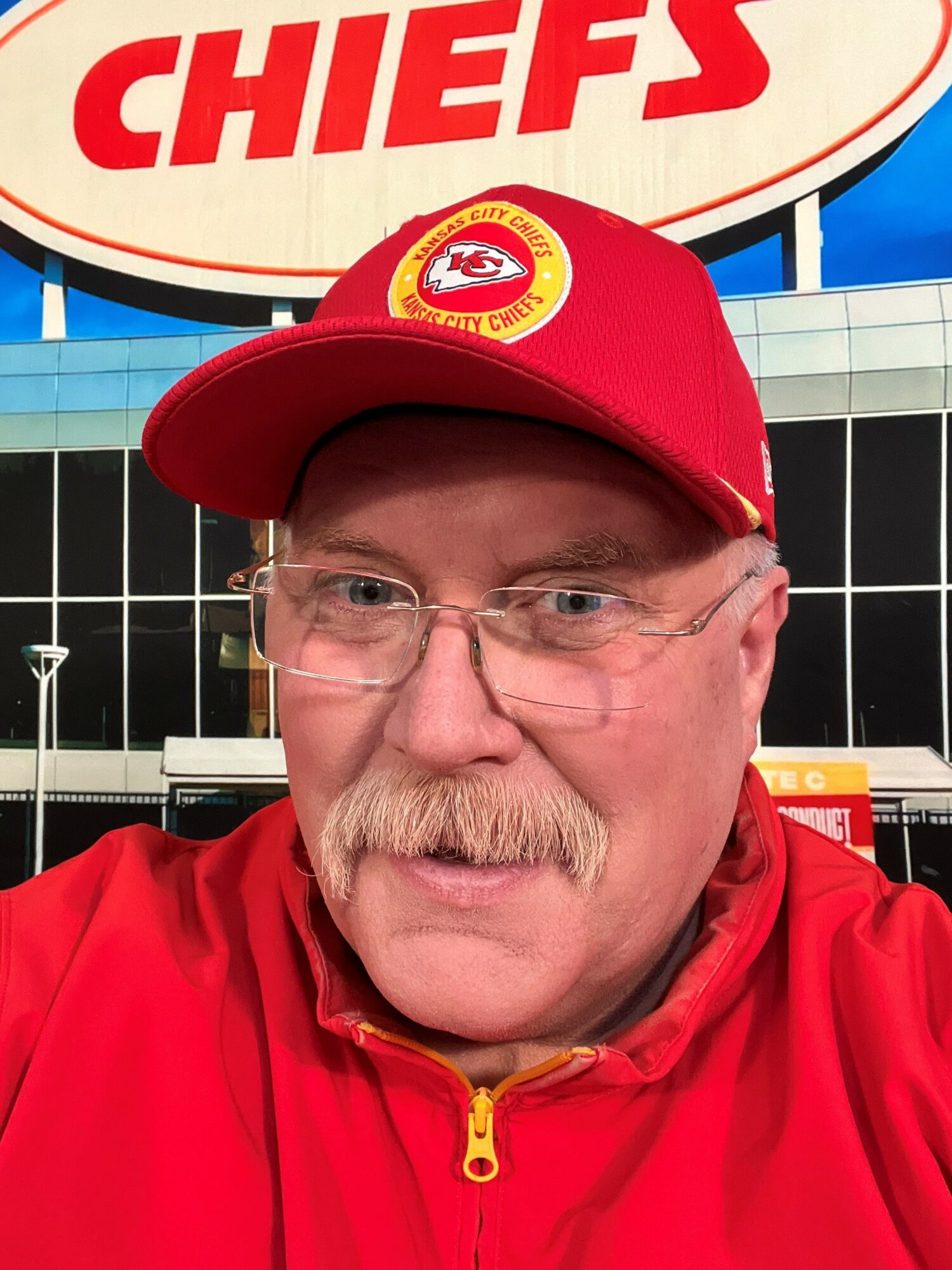 Man wearing a red cap and jacket, standing in front of a Kansas City Chiefs sign.