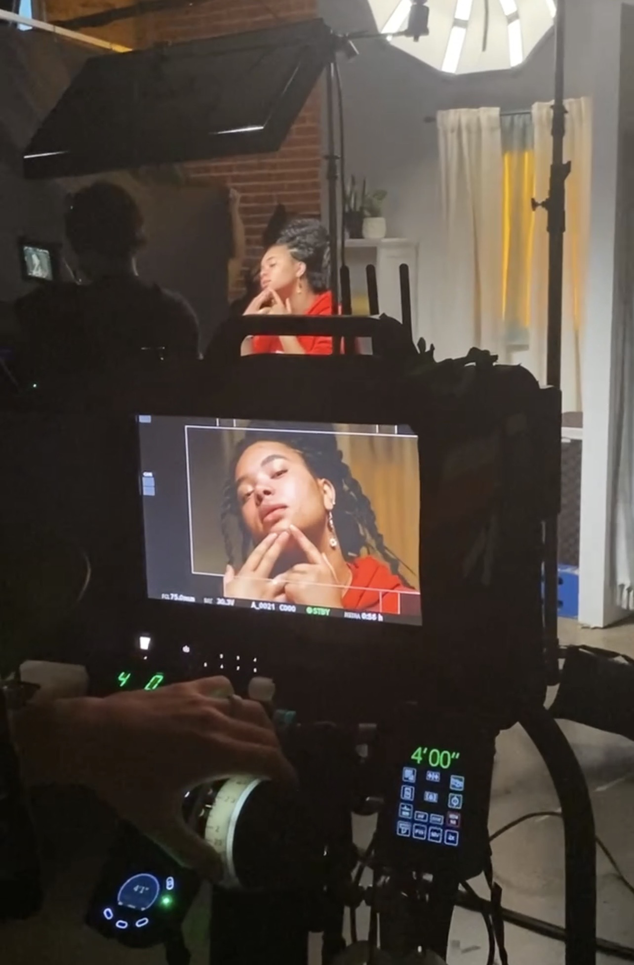 Photographer captures a woman with braided hair and red clothing, posing with her hand near her face, in a studio setting.