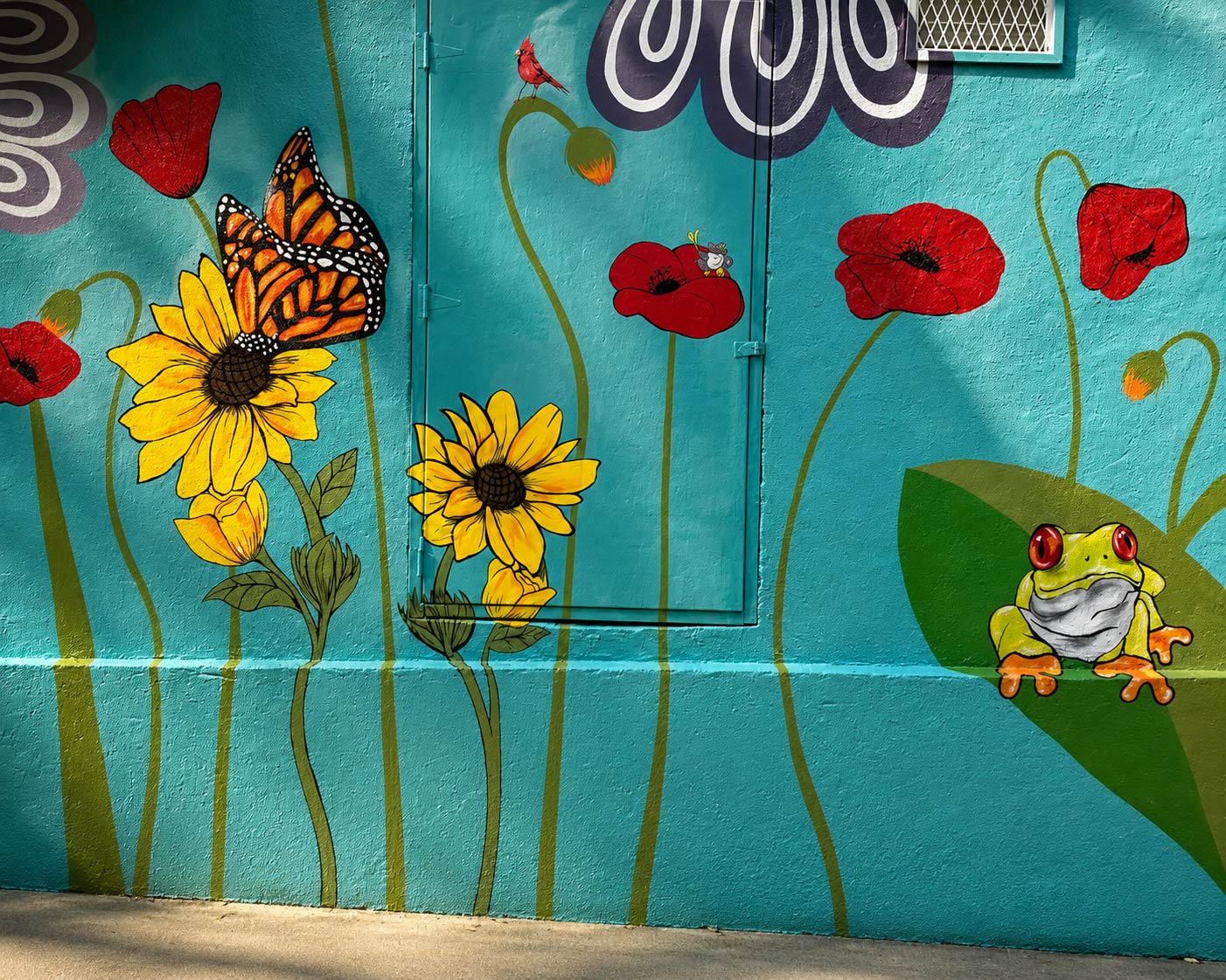 Colorful mural with sunflowers, a butterfly, red poppies, and a frog on a green leaf against a blue background.