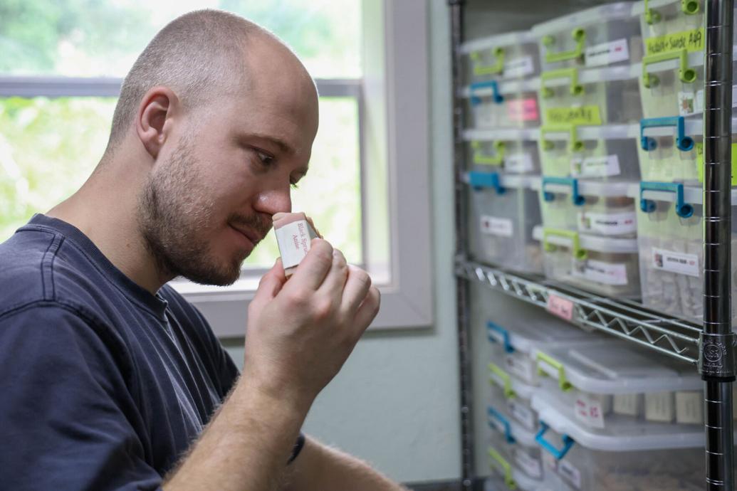 Man smelling a small container in a storage room with organized shelves and labels.