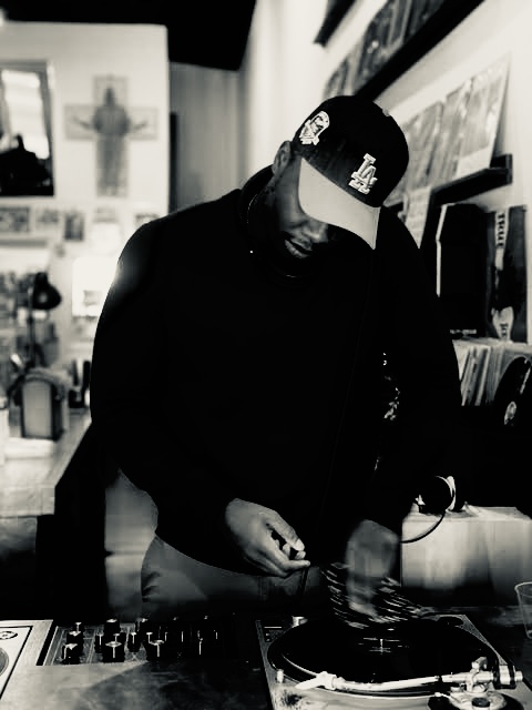 Person wearing a cap and dark clothing browsing records in a store, with shelves and posters in the background.