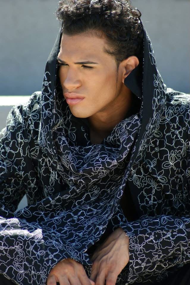 Young man with curly hair wearing a patterned hoodie, looking to the side outdoors.