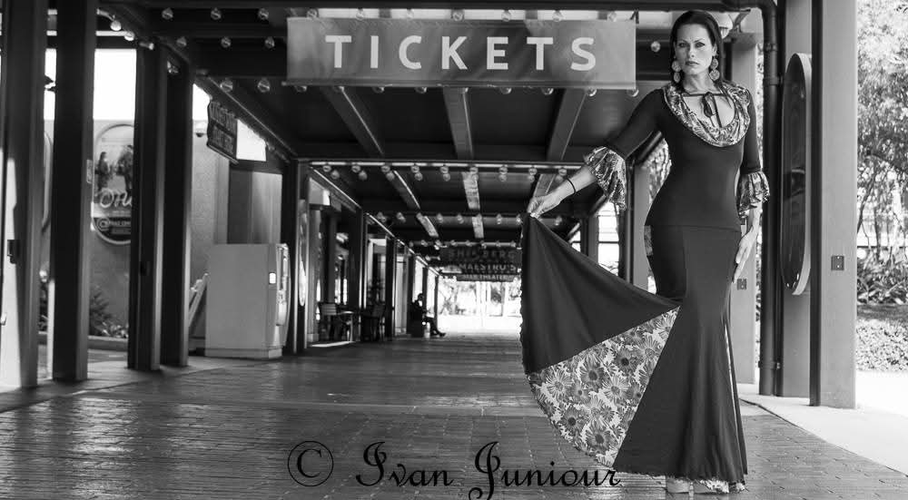 Woman in a long dress with a floral train standing under a ticket booth sign in an empty outdoor area.