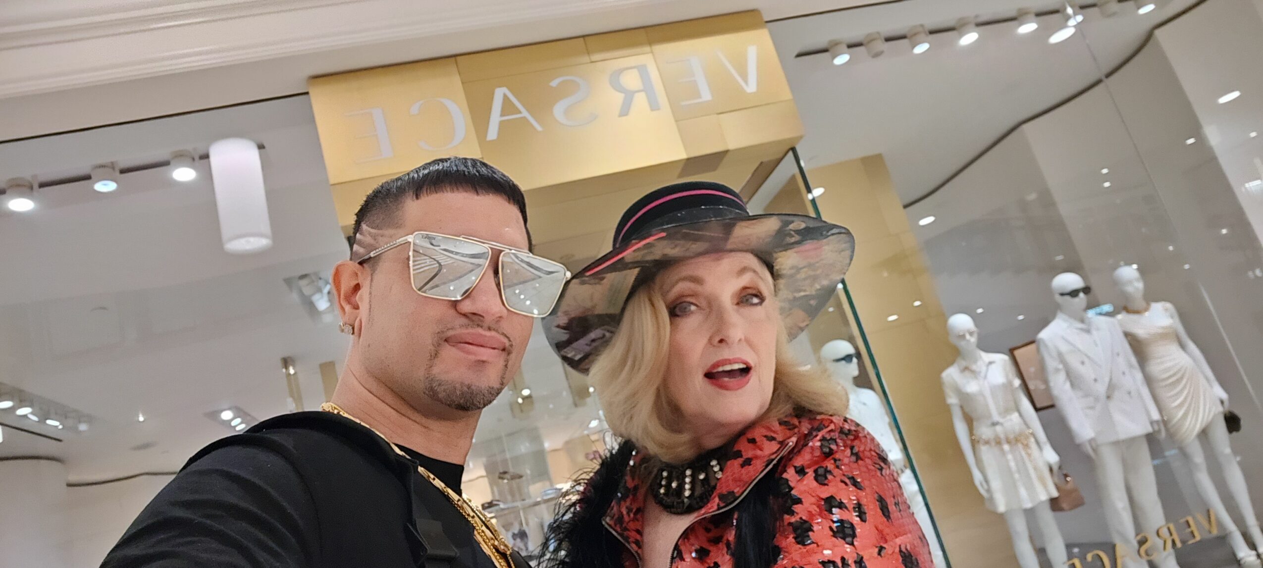 Two women taking a selfie in a store, smiling, with clothing displays in the background.