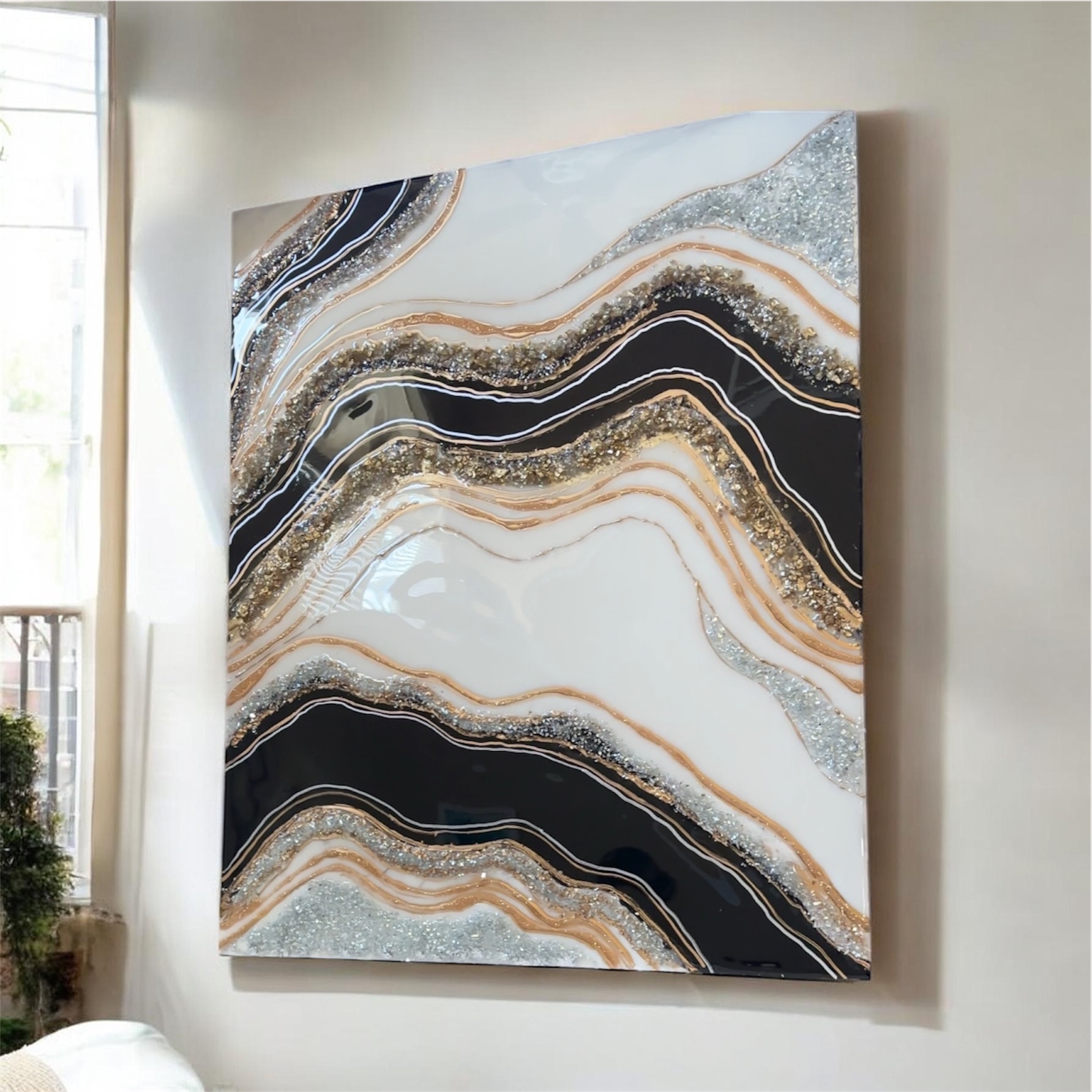 Abstract painting with wavy black, white, gold, and gray patterns on a wall, sunlight from window on left side